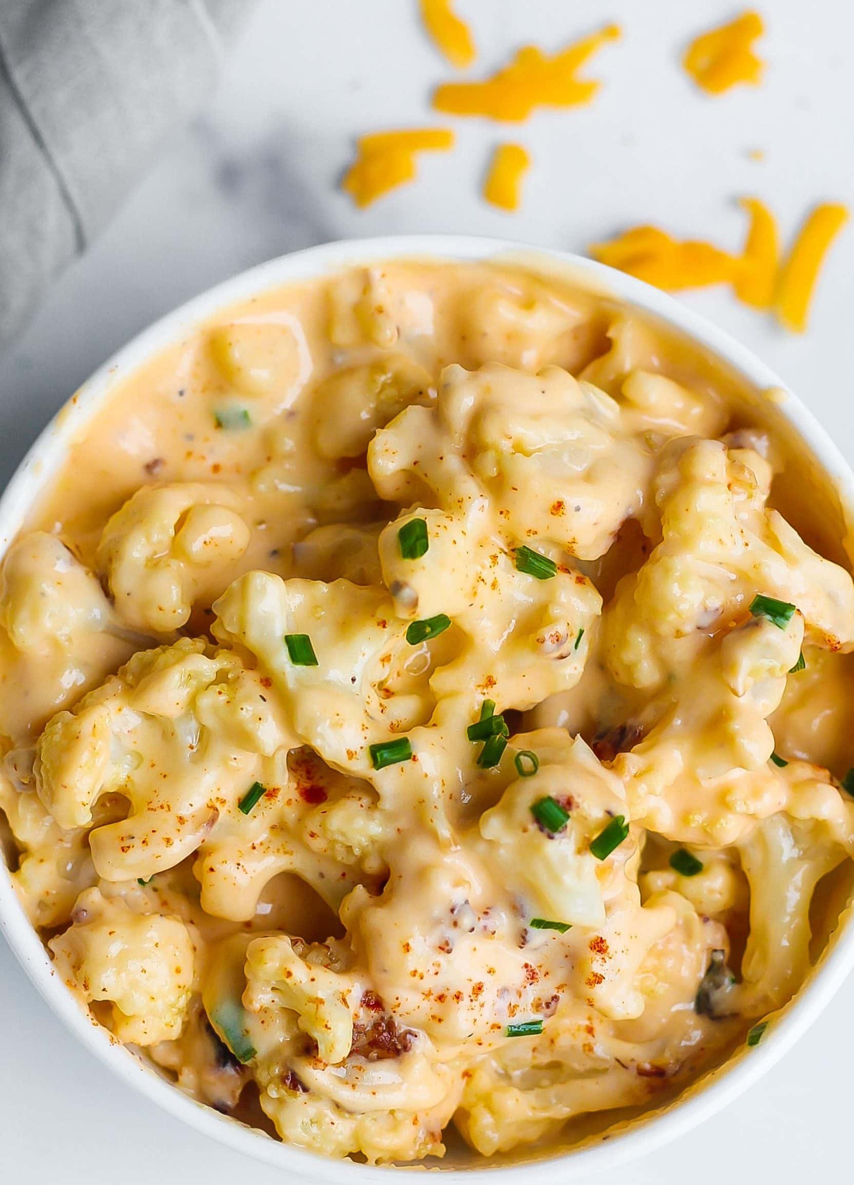 Cauliflower Mac and Cheese in a white bowl with shredded cheese in the background