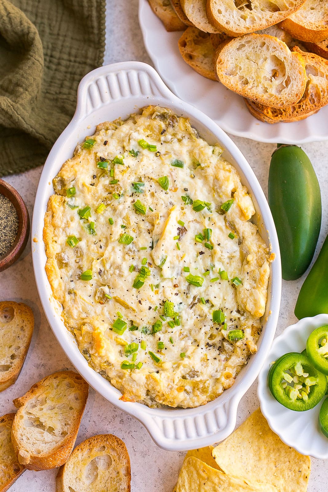 Jalapeño Artichoke Dip in a baking dish with fresh jalapenos on top.