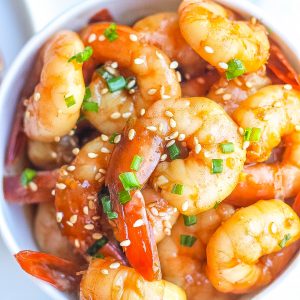 close view of honey garlic shrimp in bowl topped with sesame seeds and green onions