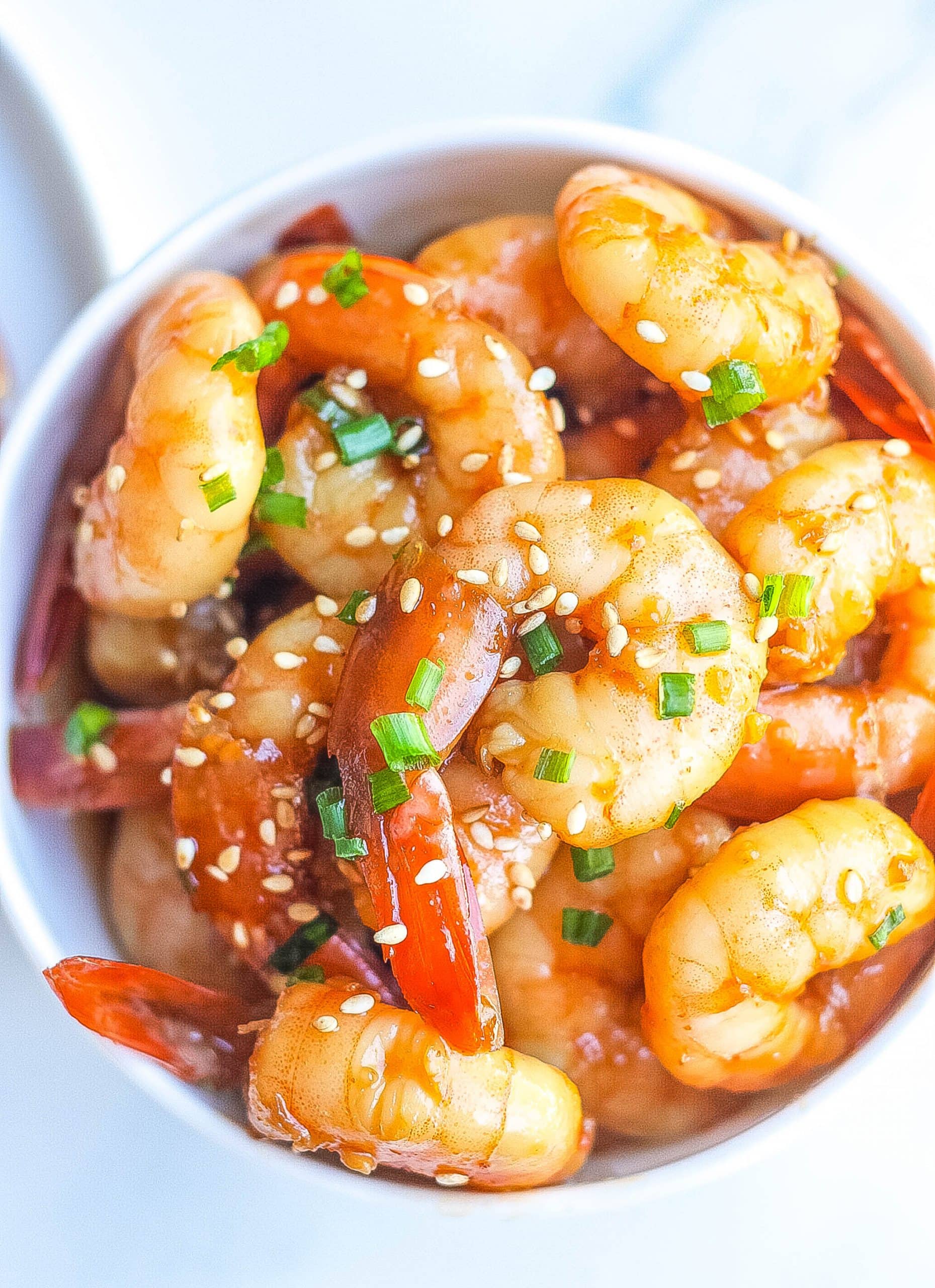 close view of honey garlic shrimp in bowl topped with sesame seeds and green onions