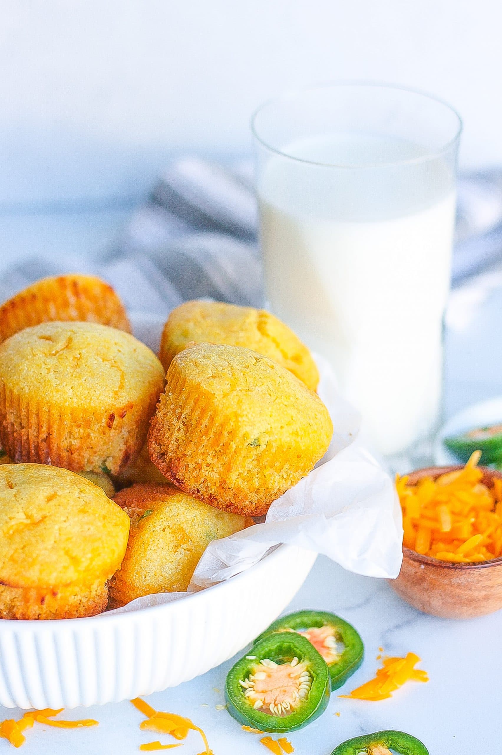 one bowl of jalapeño cheddar cornbread muffins with slices of jalapeños and a glass of milk