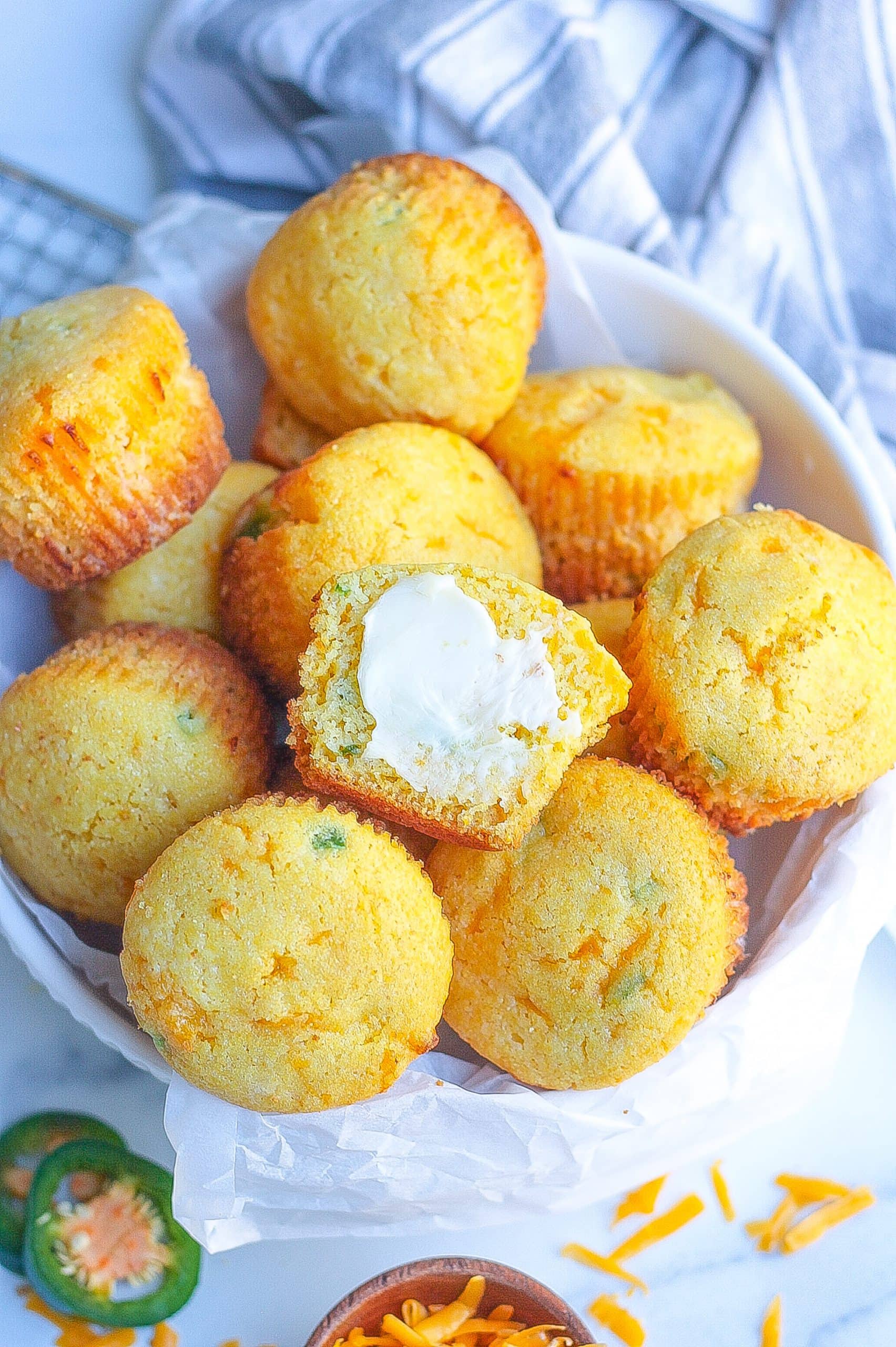 one white bowl filled with jalapeño cornbread muffins with one covered in butter