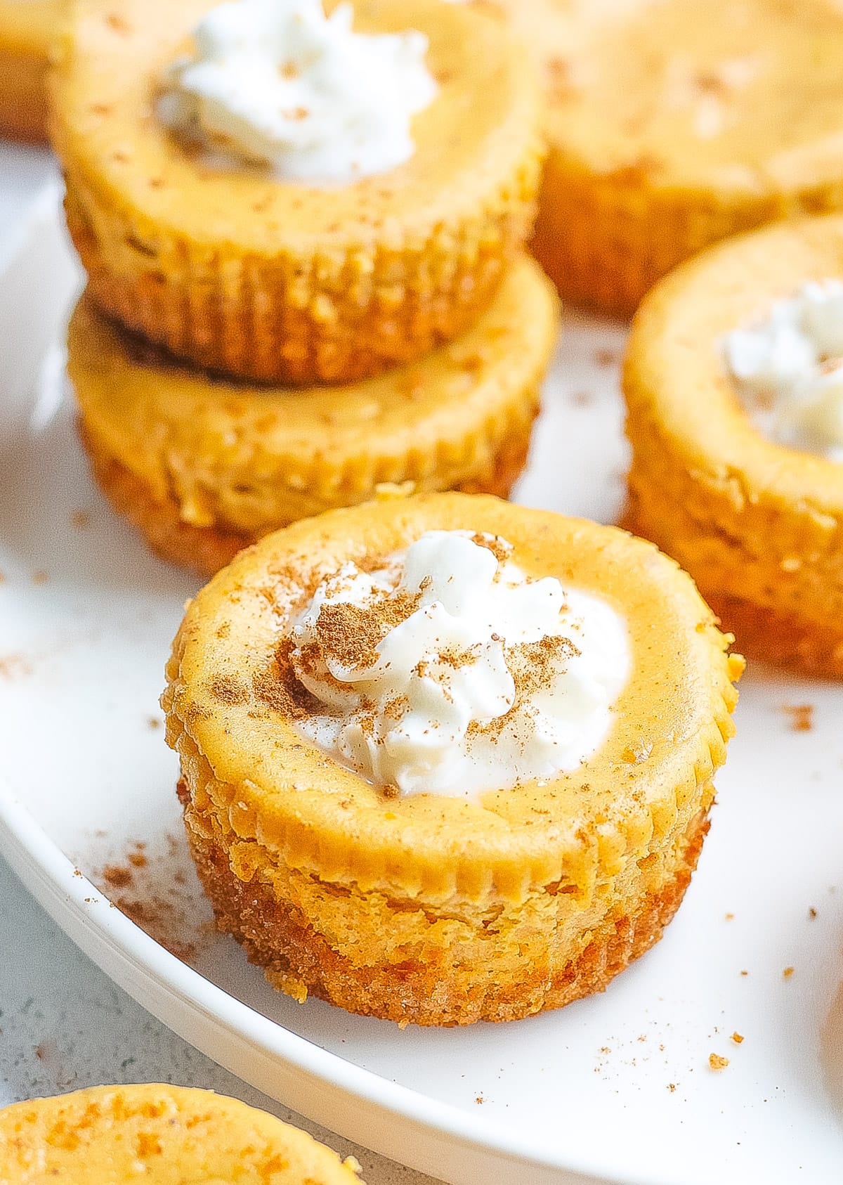three mini pumpkin pie cheesecake bites on white plate with whipped cream and spices