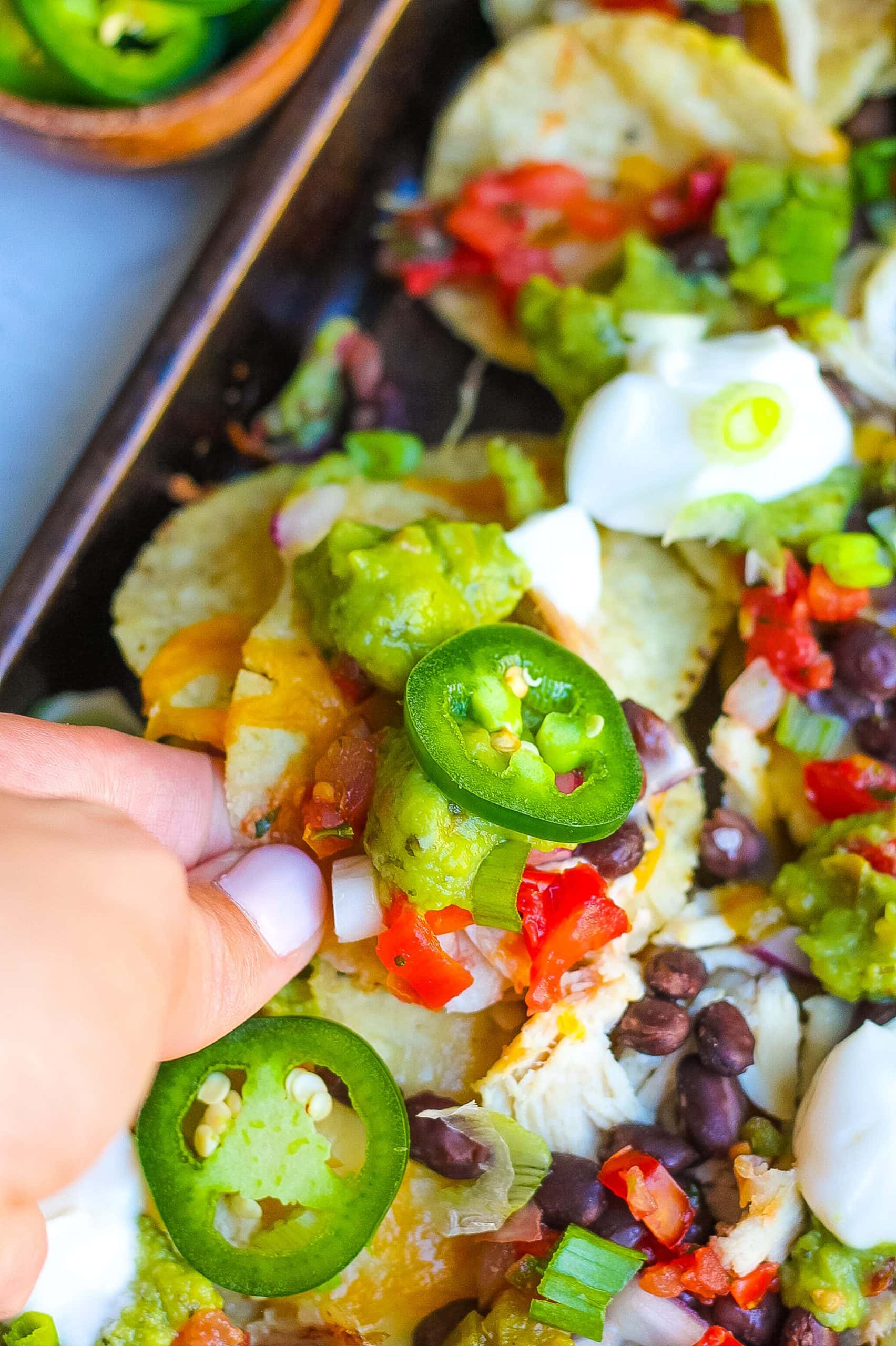 close view of scooping a nacho with jalapeńo, pico de gallo, cheese