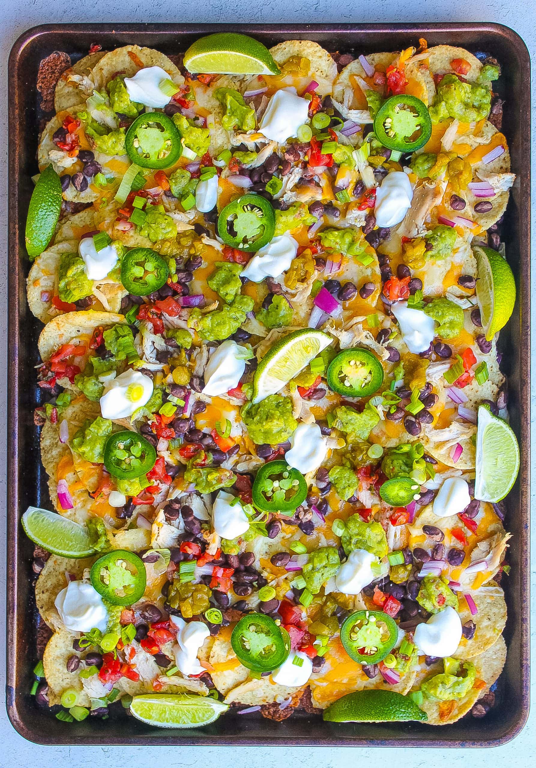 baked sheet pan chicken nachos with sour cream, cheese, black beans, guacamole, jalapeńo, lime