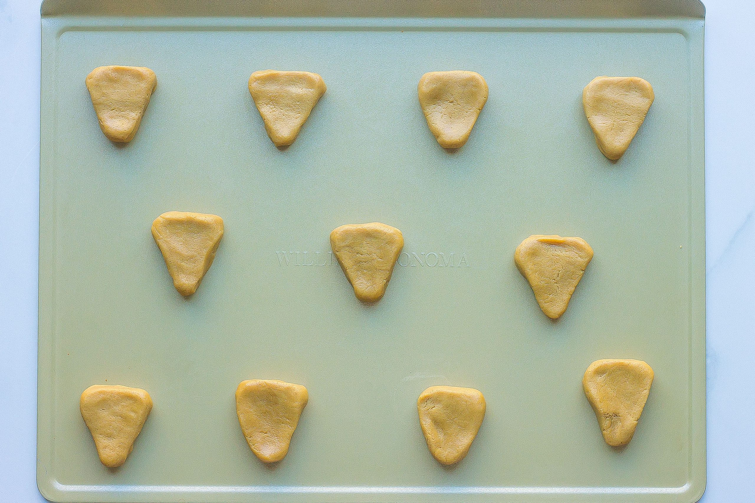 Peanut butter cookie dough shaped into triangles on cookie sheet