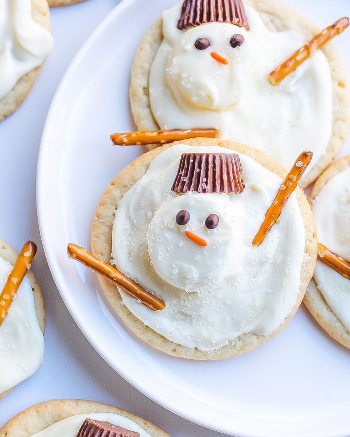 melted snowman cookies on white plate with Reese's, pretzels, marshmallows, and sparkling sugar