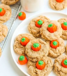 Spice cookies with pumpkin candies on circular white plate.