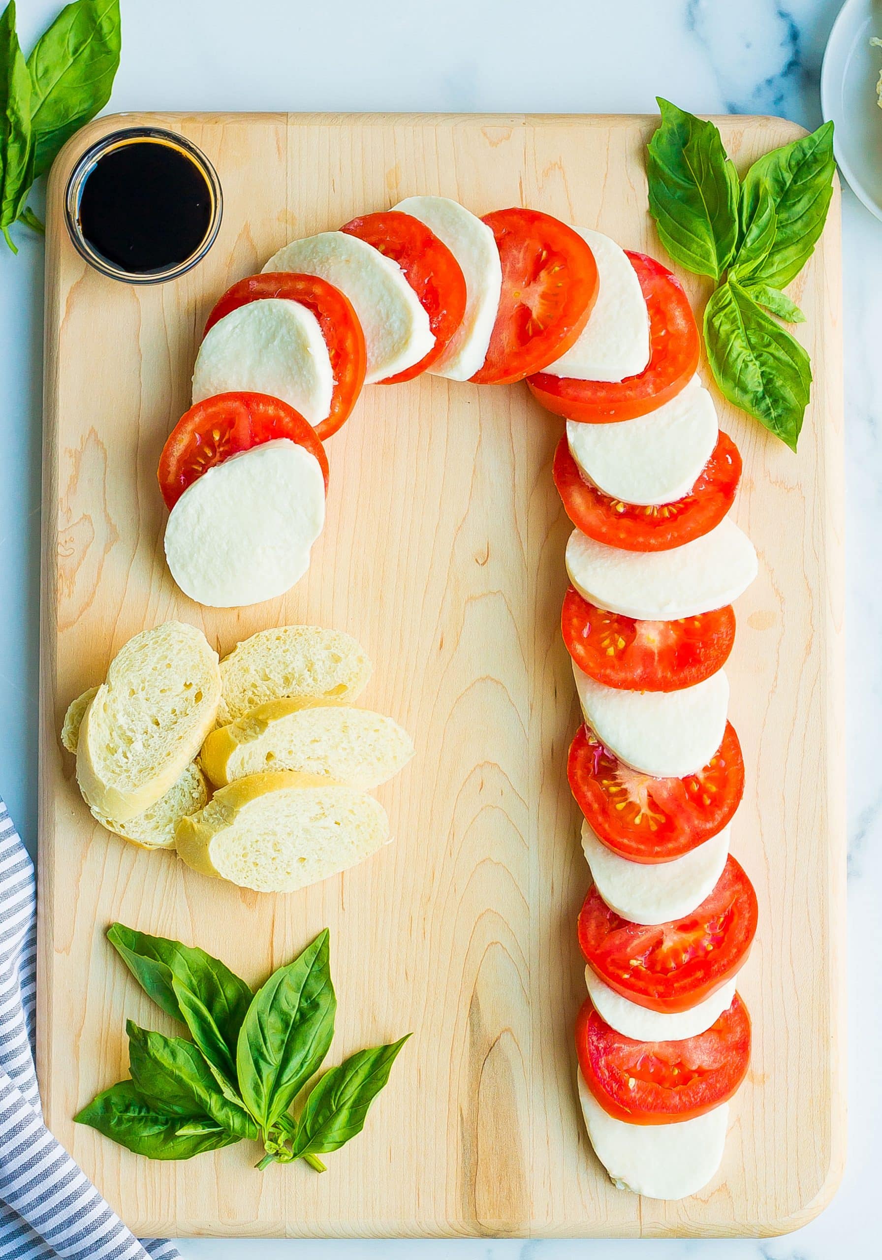sliced tomato and mozzarella on wooden cutting board with basil and bread