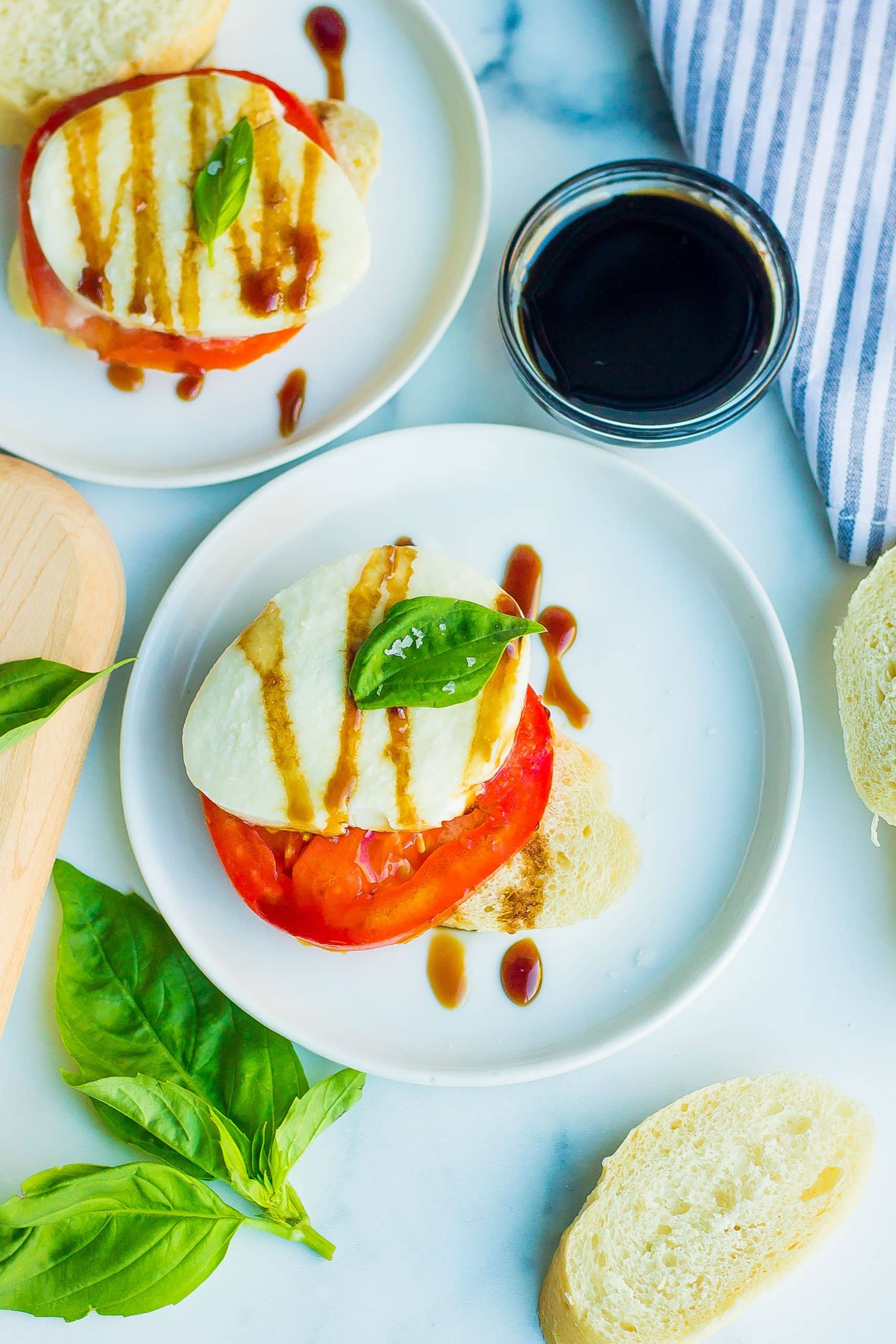 caprese salad with basil and balsamic on white plates with bread 
