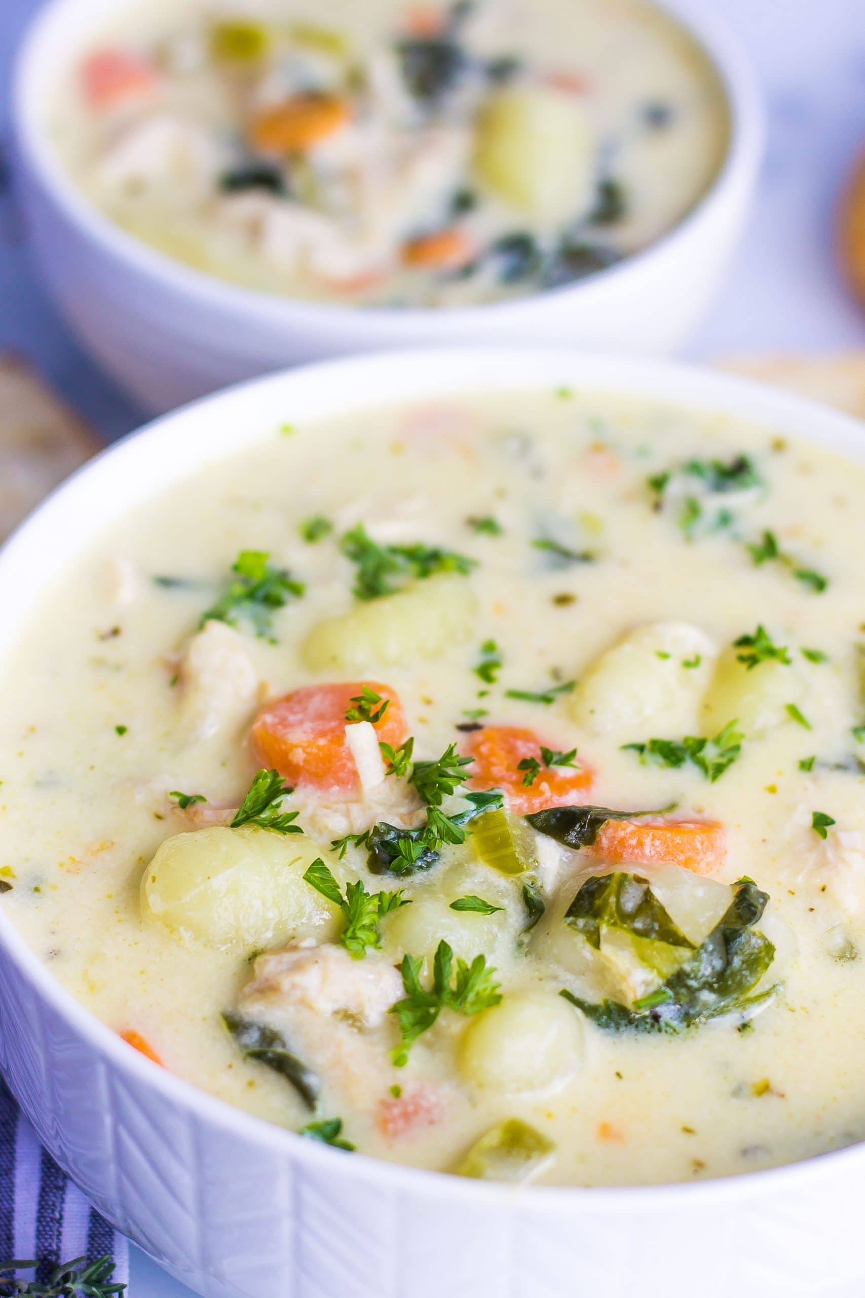 two white bowls of chicken gnocchi soup with fresh herbs
