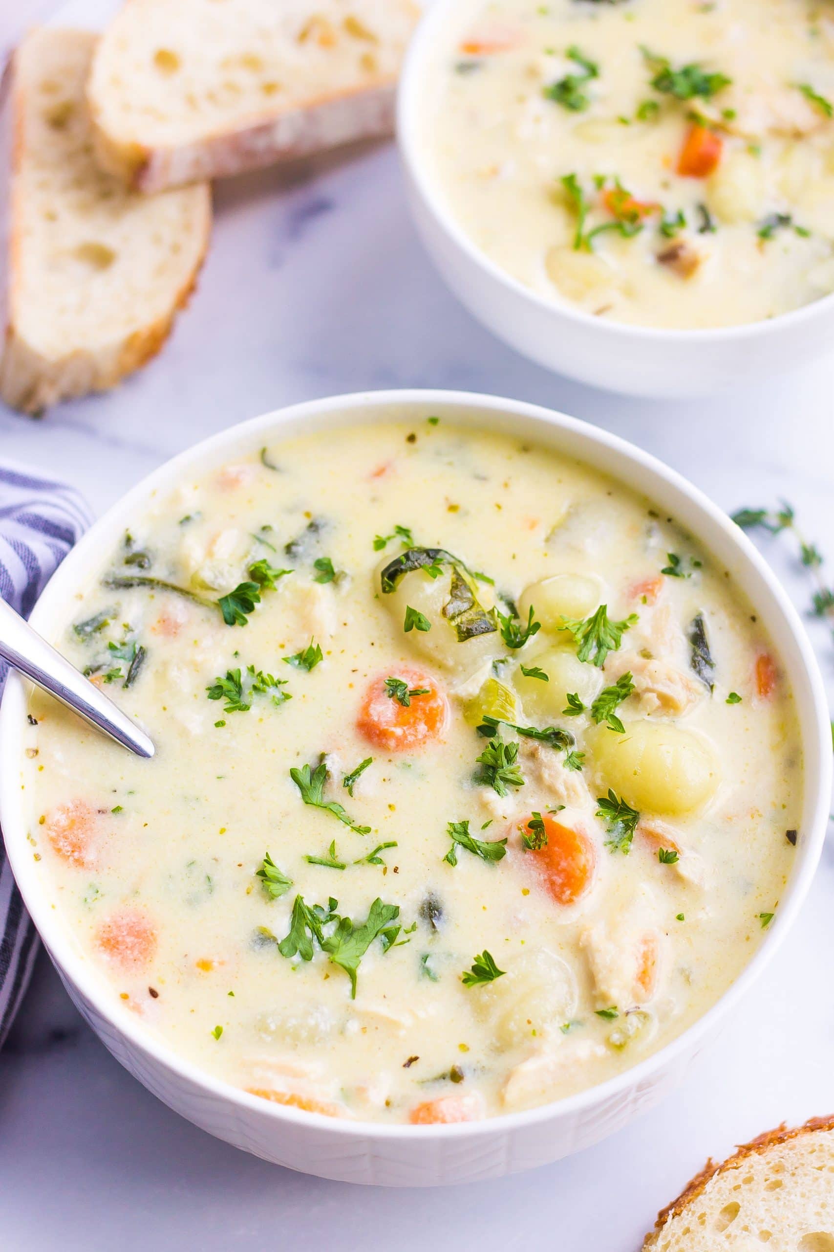 two bowls of gnocchi soup with chicken, carrots, celery, herbs