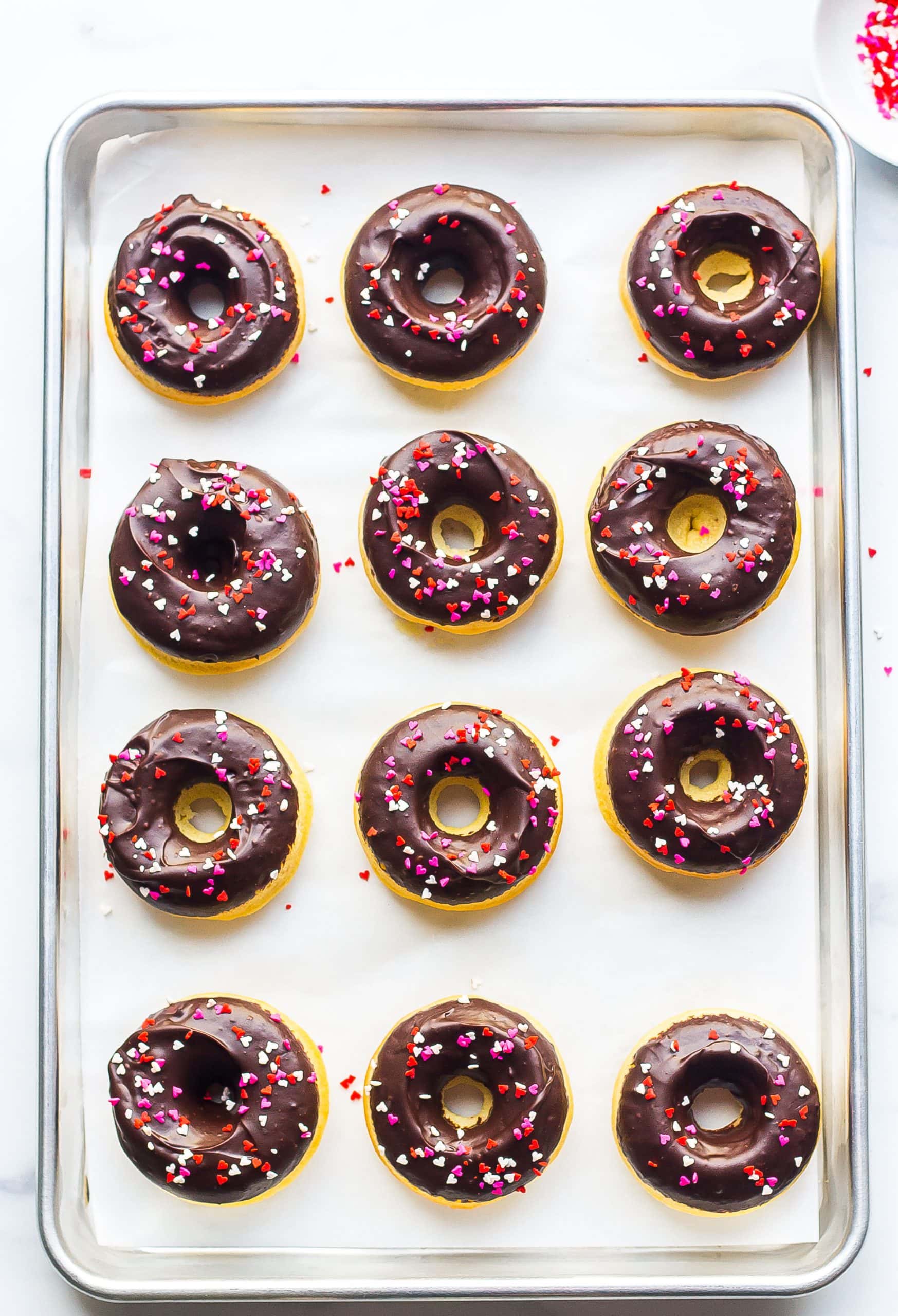 frosted baked donuts on baking sheet with sprinkles