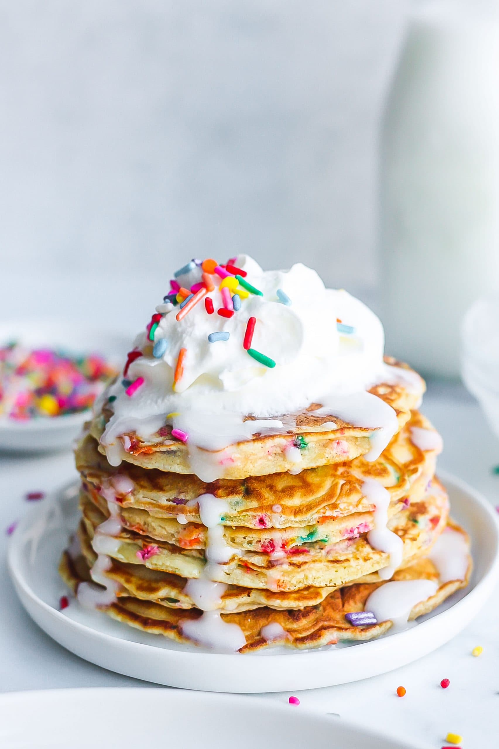 tall stack of funfetti pancakes with whipped cream and icing dripping on the sides