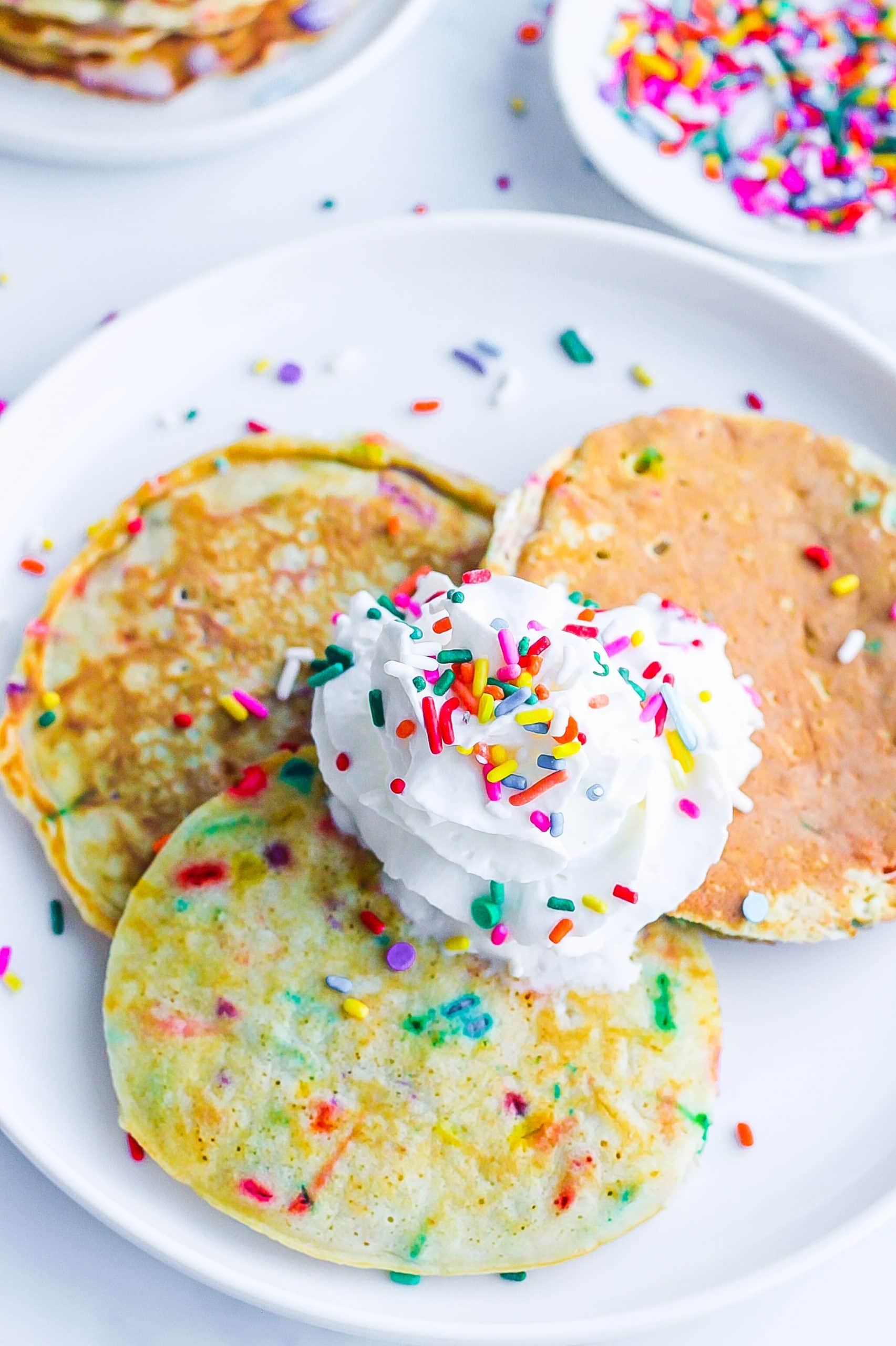 plate of pancakes with sprinkles topped with whipped cream