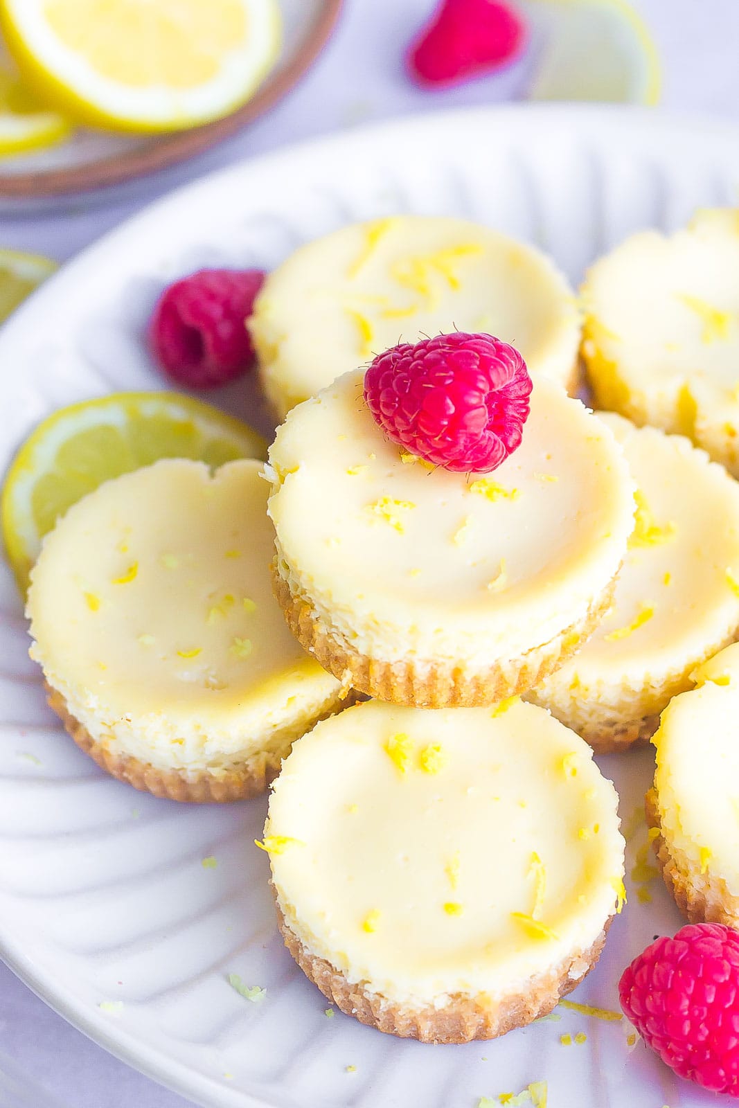 mini lemon cheesecakes on a white plate with raspberries on top