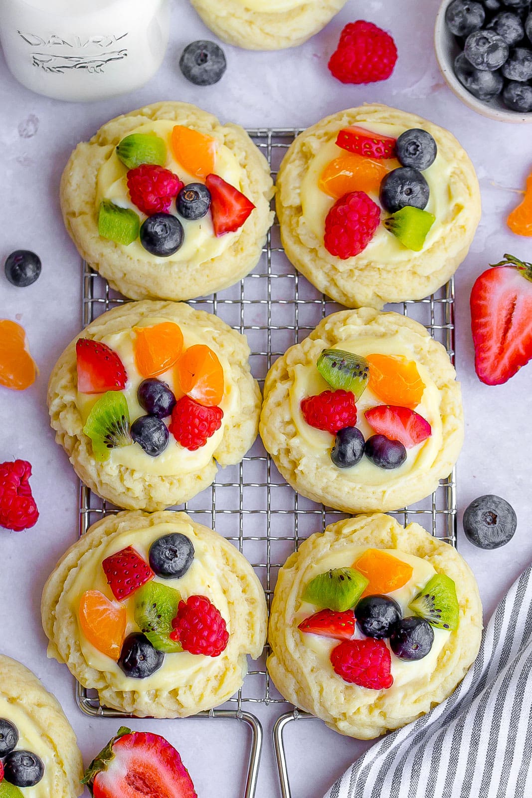fruit pizza cookies on cooling rack with fresh fruit and glass of milk