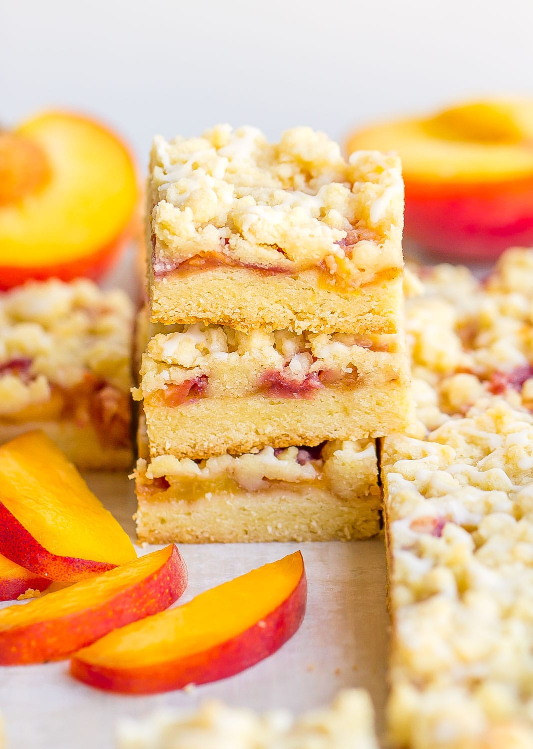 Peach Crumble Bars stacked on top with fresh peaches
