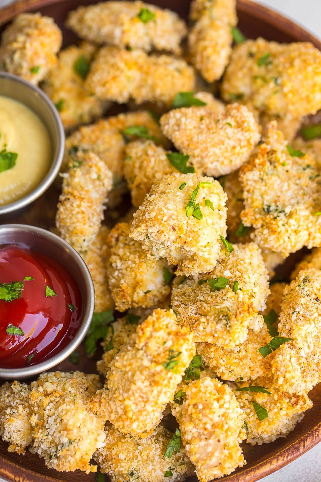 close up view of crispy chicken nuggets with a ramekin of ketchup and hone mustard. 