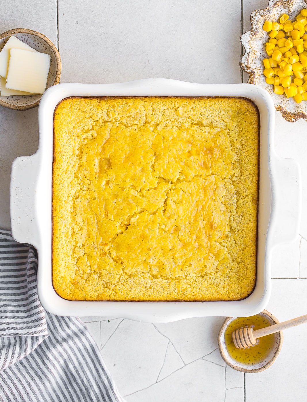 Birdseye view of the best Cornbread Pudding with honey, butter and corn on the side.