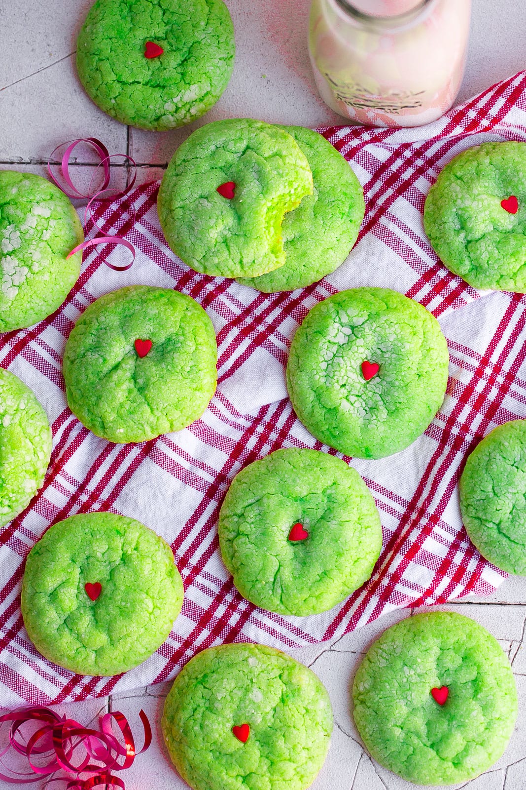 Green Grinch cookies on a red and white plaid kitchen towel.