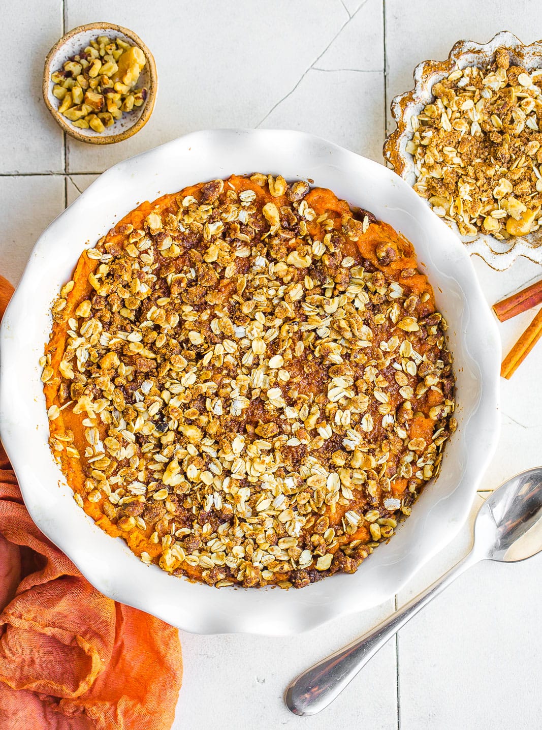 Birdseye view of sweet potato casserole recipe with oat crumble topping, cinnamons stick, and serving spoon.