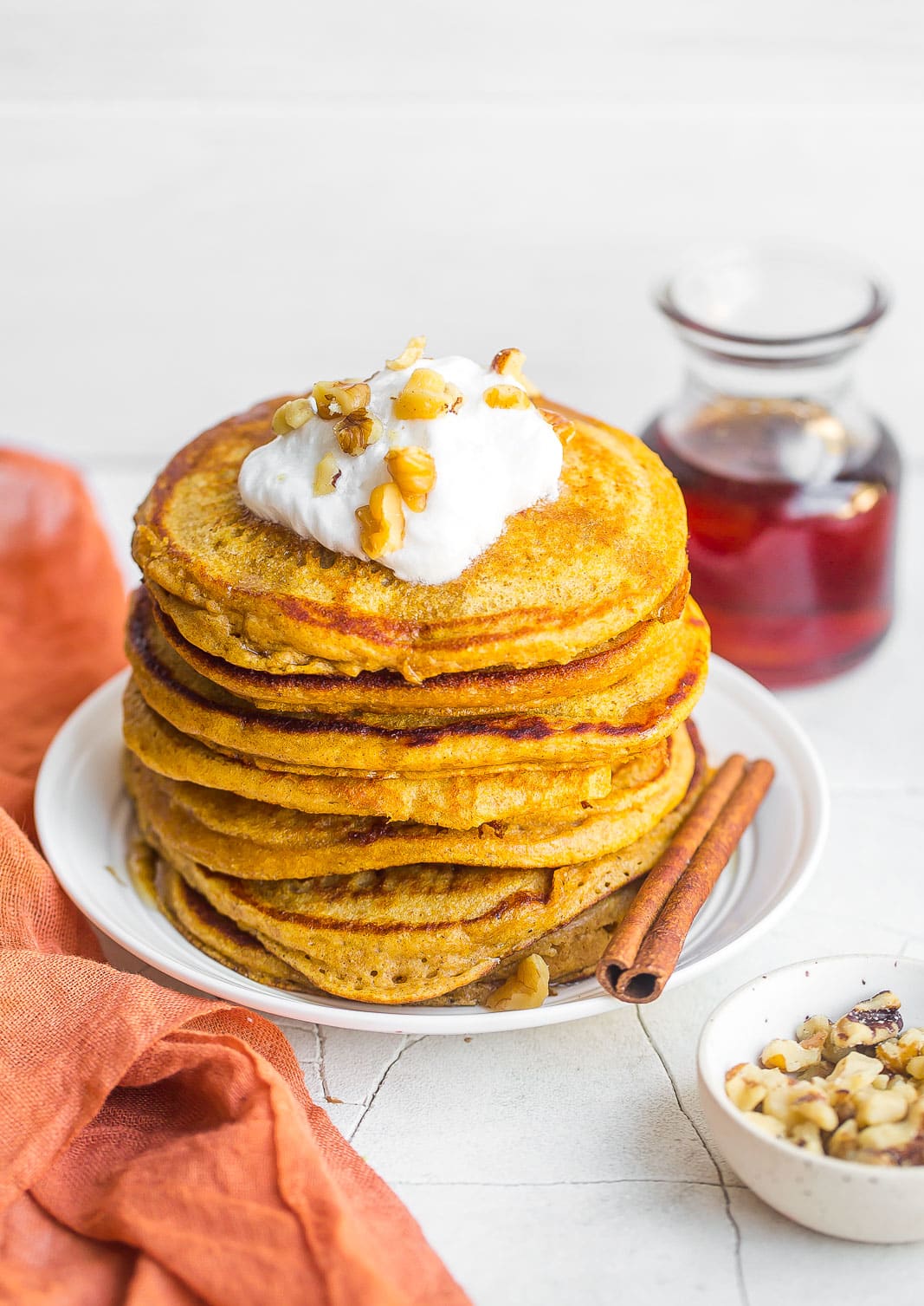 A tall stack of Pumpkin Spice Pancakes with whipped cream on top.
