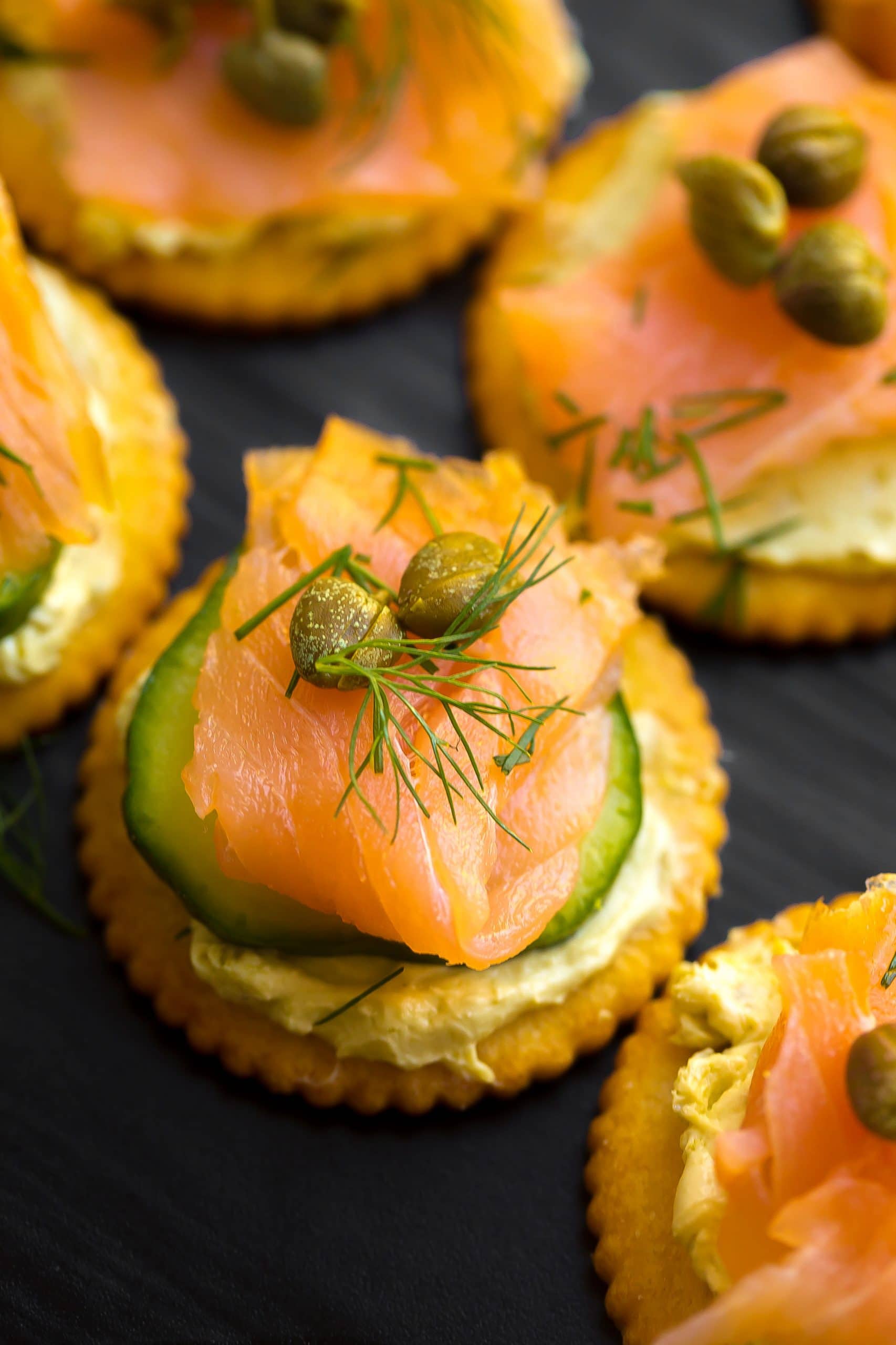 Side angle view of smoked salmon on a cracker with cucumber, capers and dill.