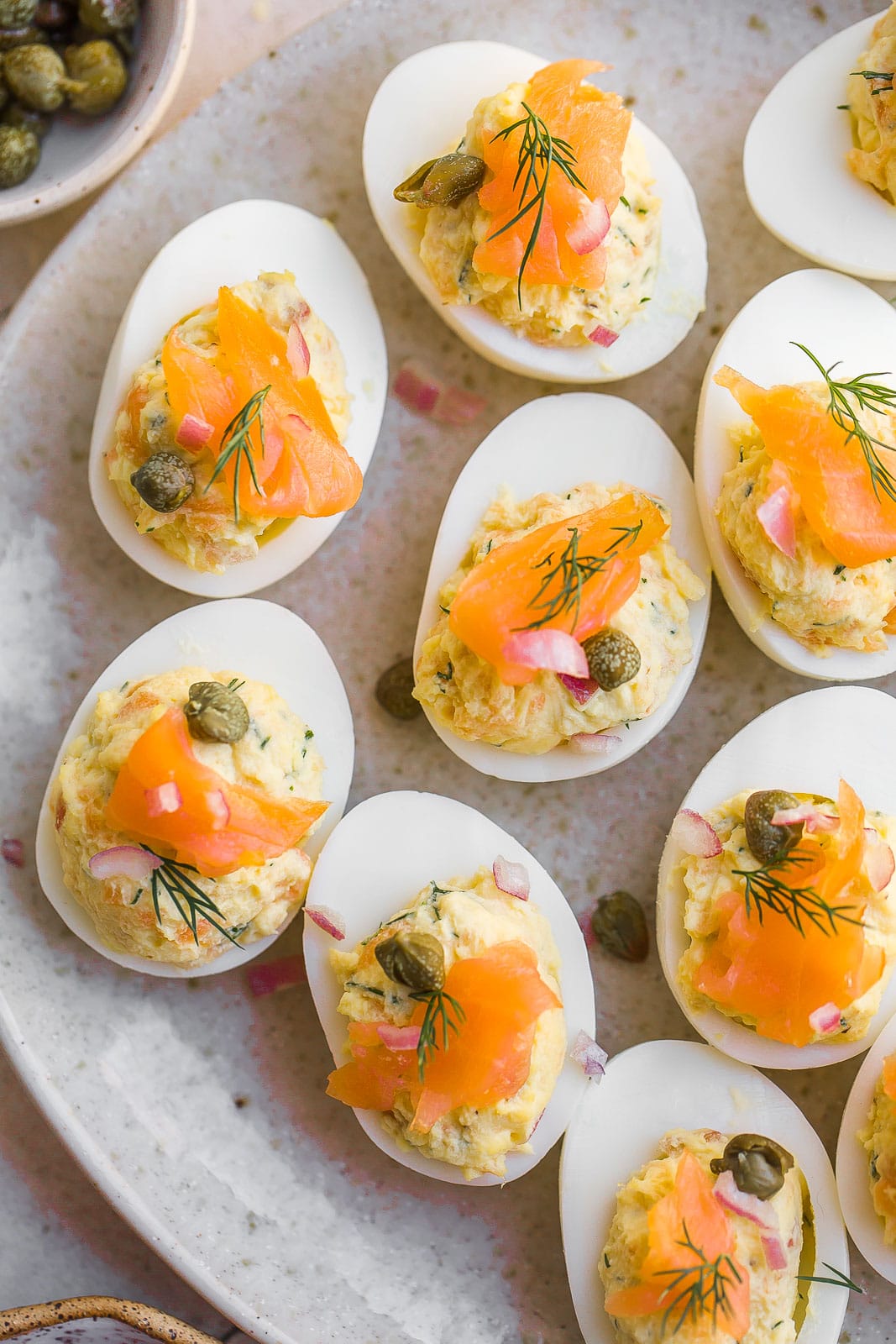 Plate full of eggs with smoked salmon and capers on top;.