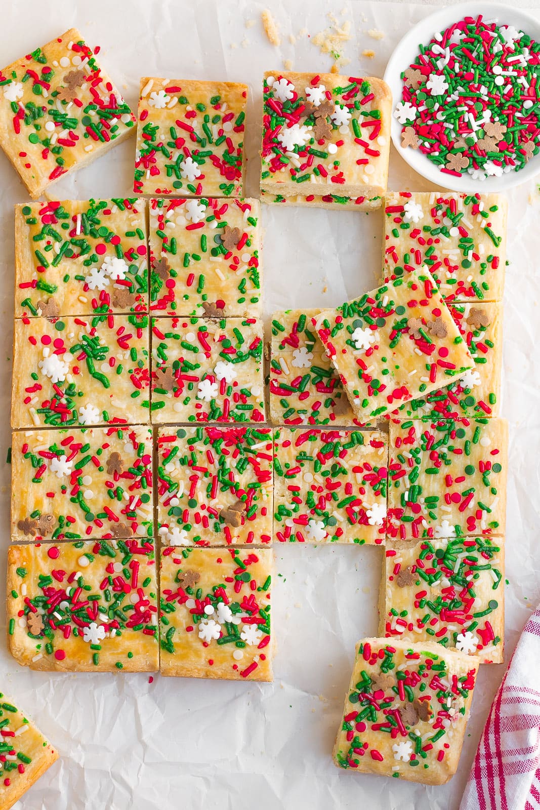 Shortbread Cookie Bars with Christmas sprinkles cut up into squares on parchment paper. 