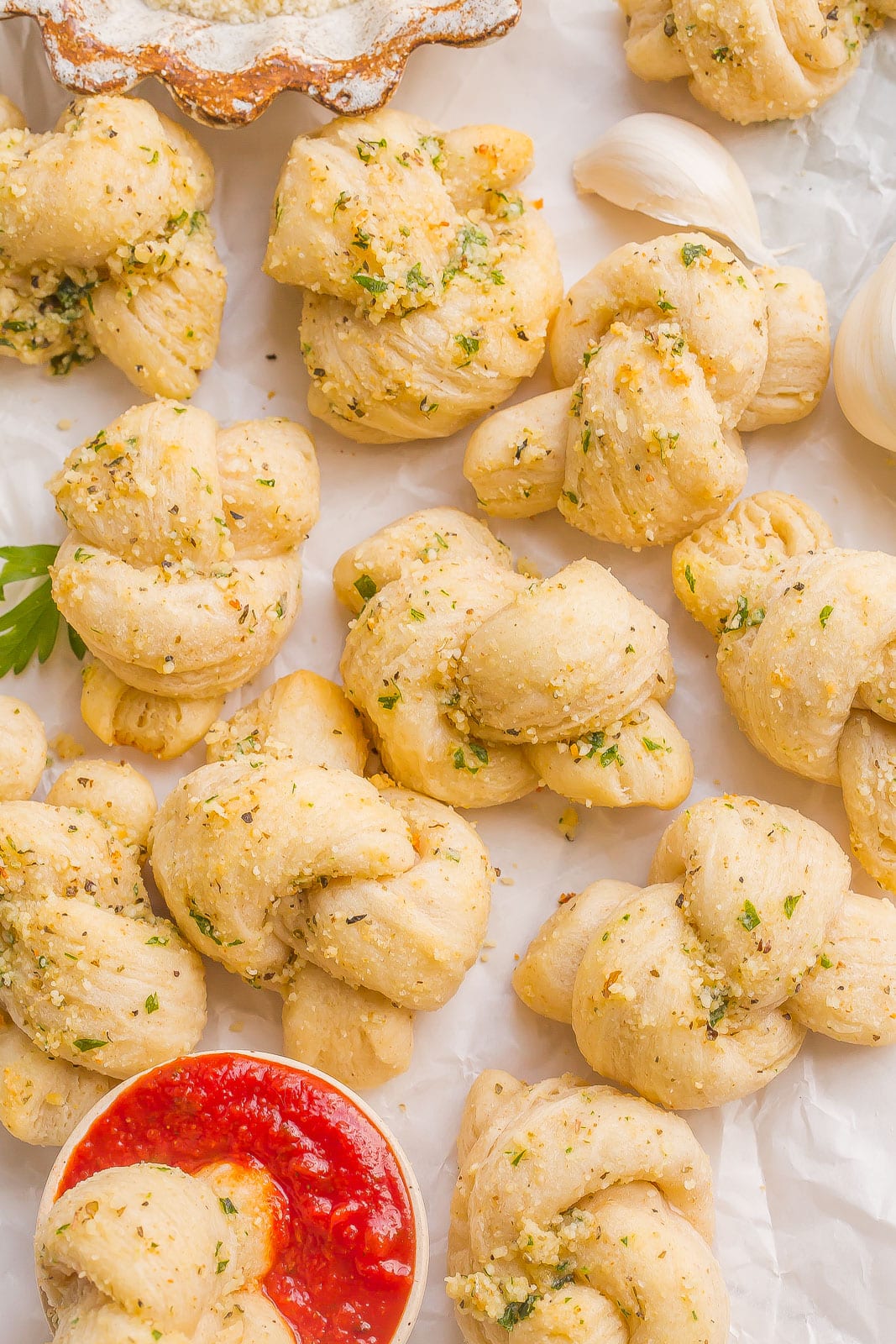 Garlic Knots on parchment paper with garlic cloves.