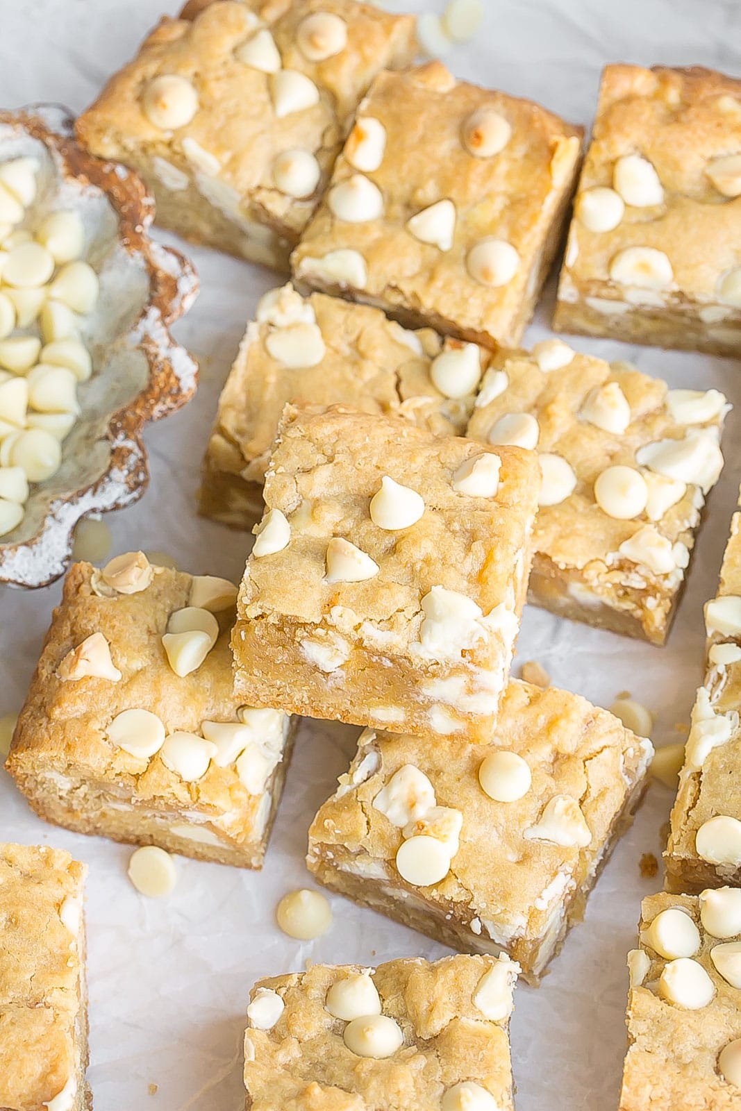 Blondies with white chocolate all cut out into squares on parchment paper.