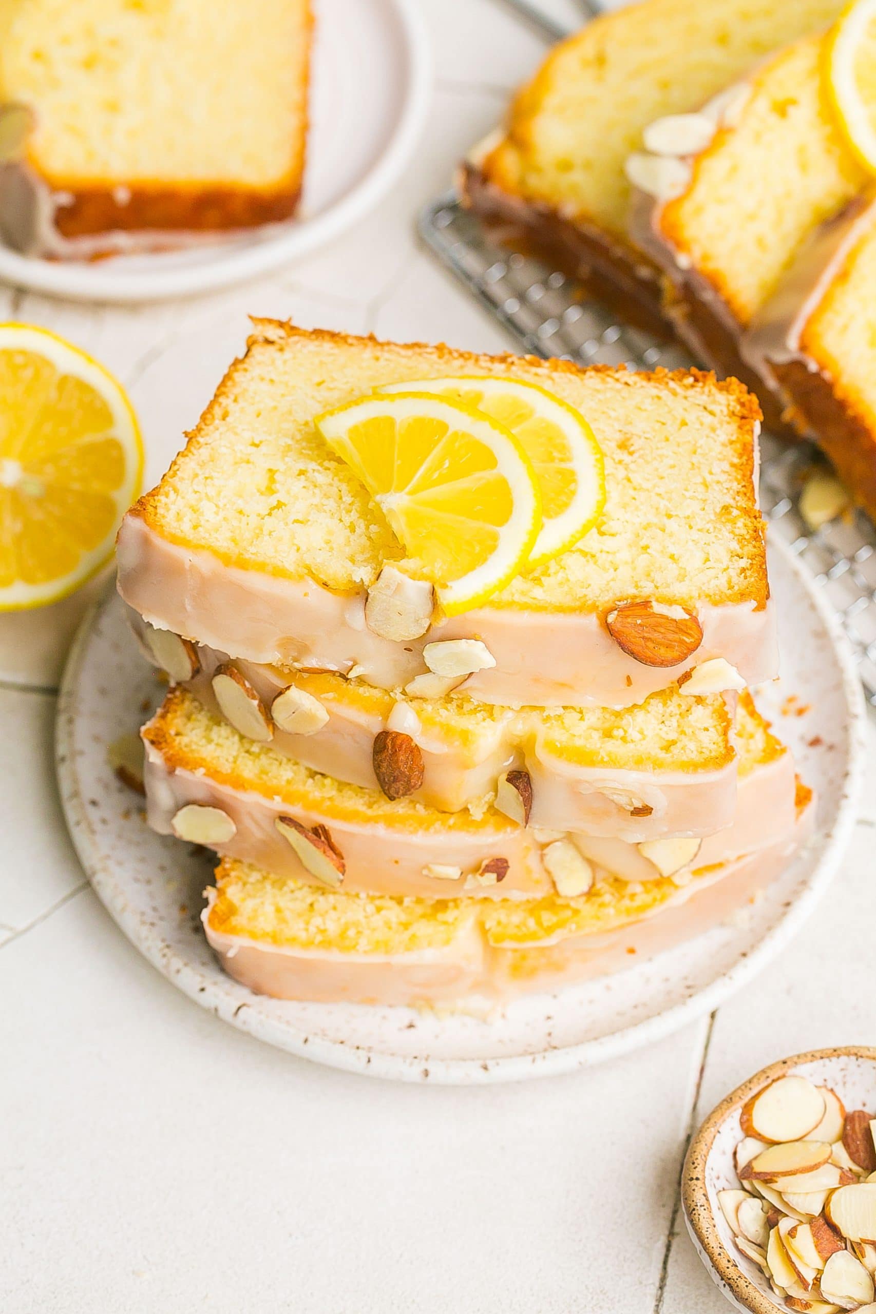 Stack of sliced iced cake with lemon an almonds on plate. 