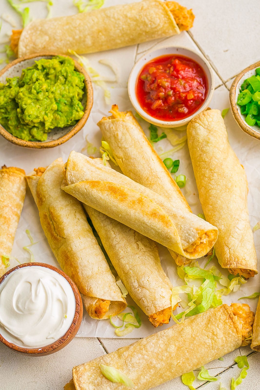 Chicken taquitos on parchment paper with guacamole, salsa and green onions. 
