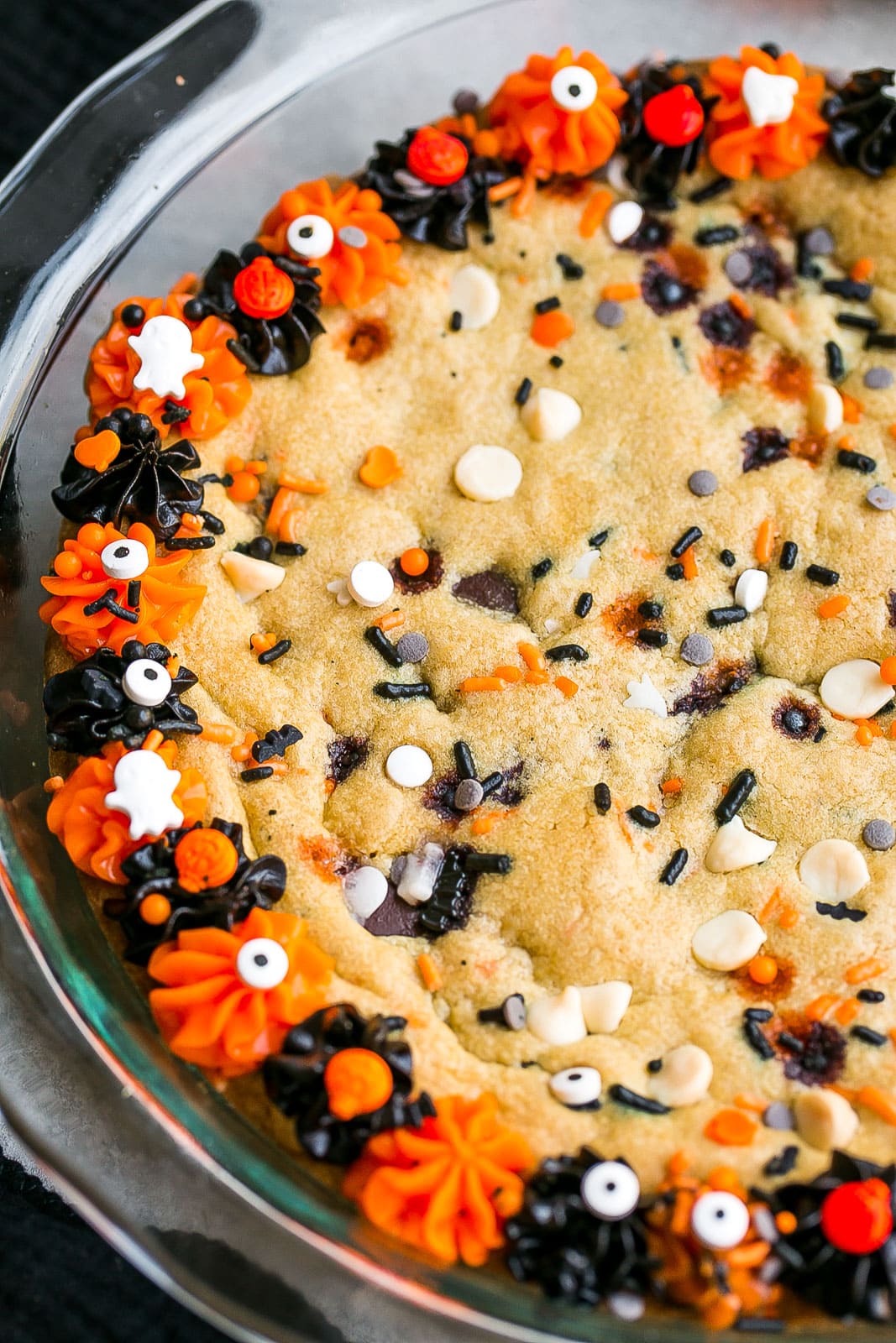 Side of cookie cake with black and orange sprinkles and frosting.