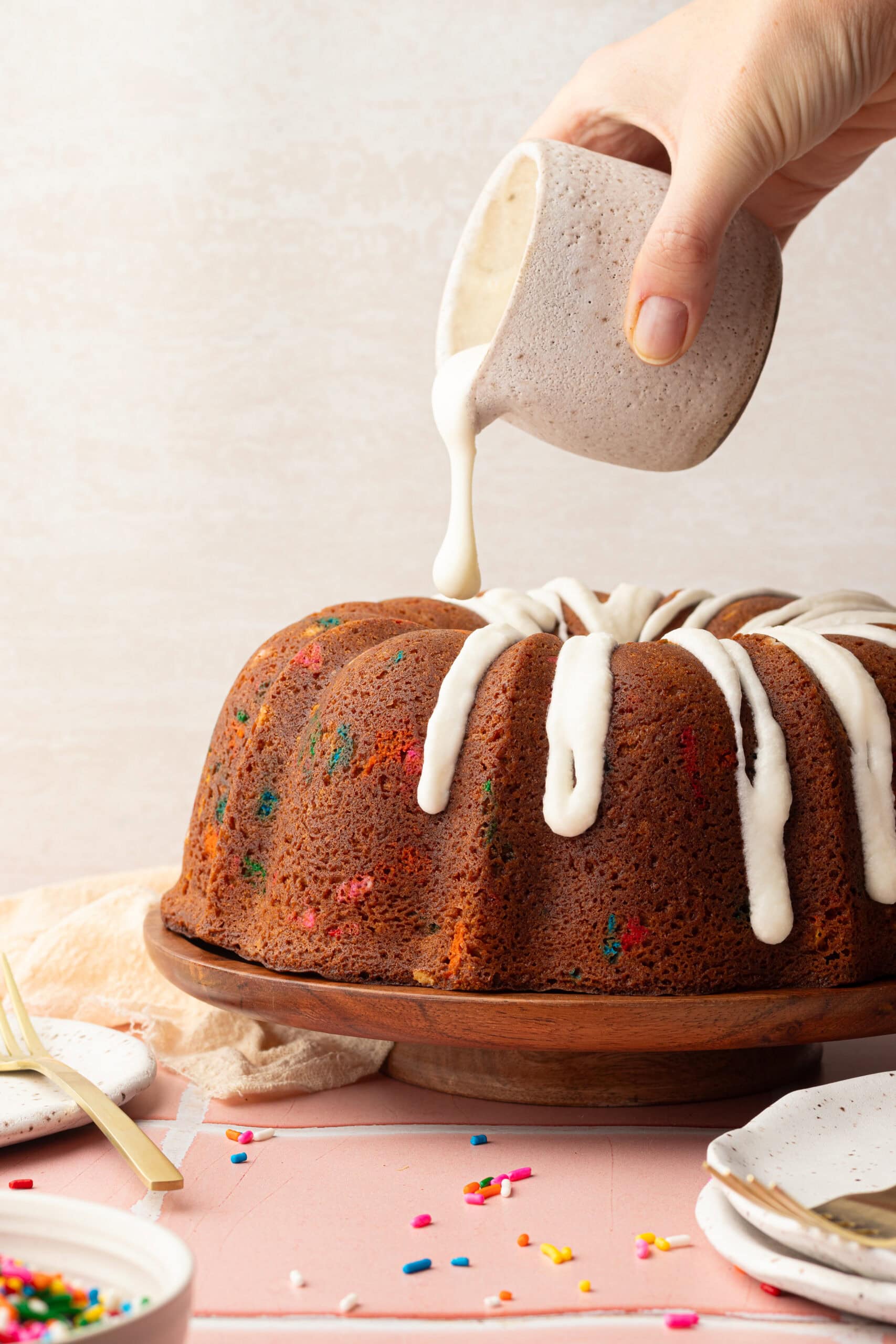 Vanilla buttercream icing getting poured on top of a sprinkled bundt cake.