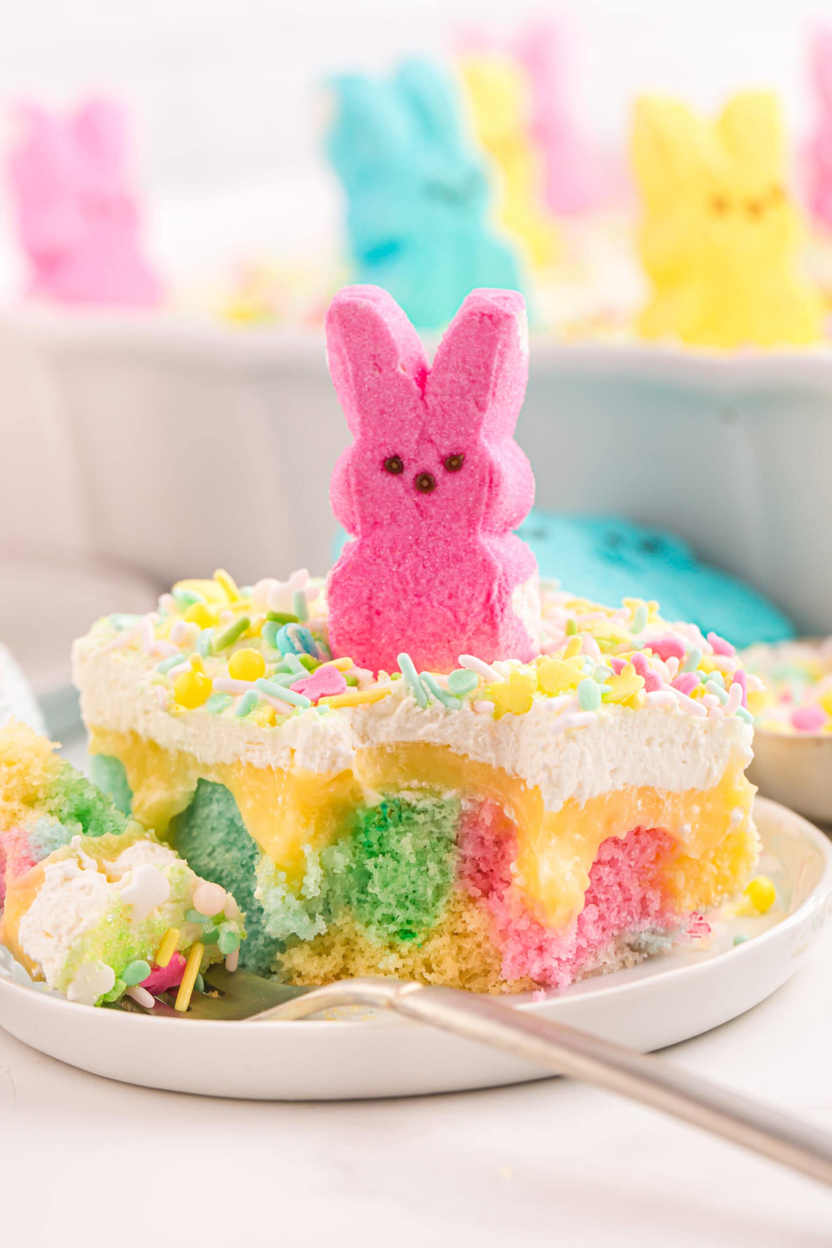 Colorful Easter Poke Cake with pink marshmallow bunny on top.