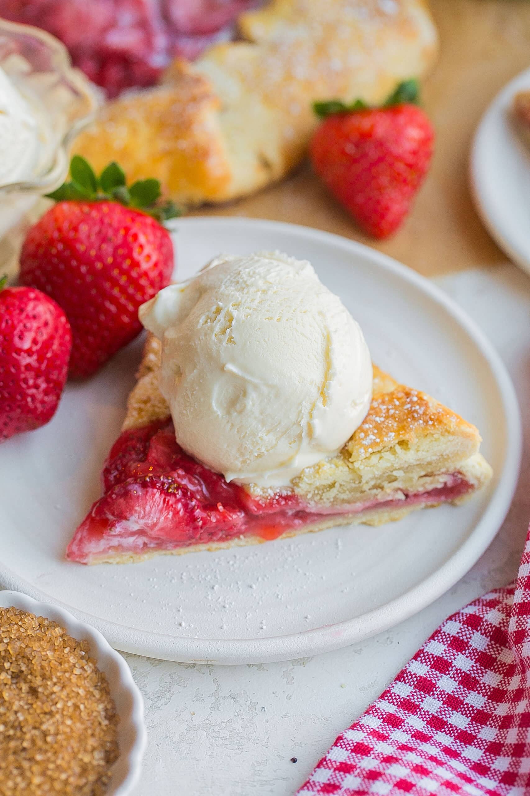 A slice of rustic strawberry tart with vanilla ice cream on top.