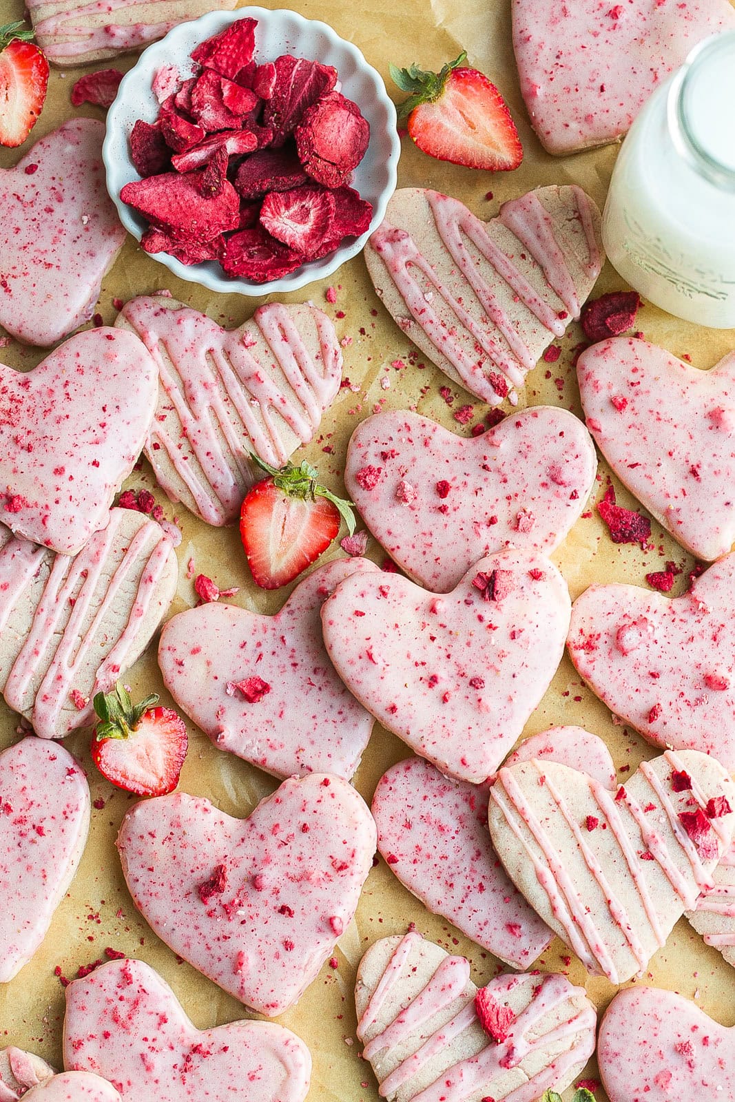 A batch of easy strawberry shortbread cookies with icing on parchment paper.