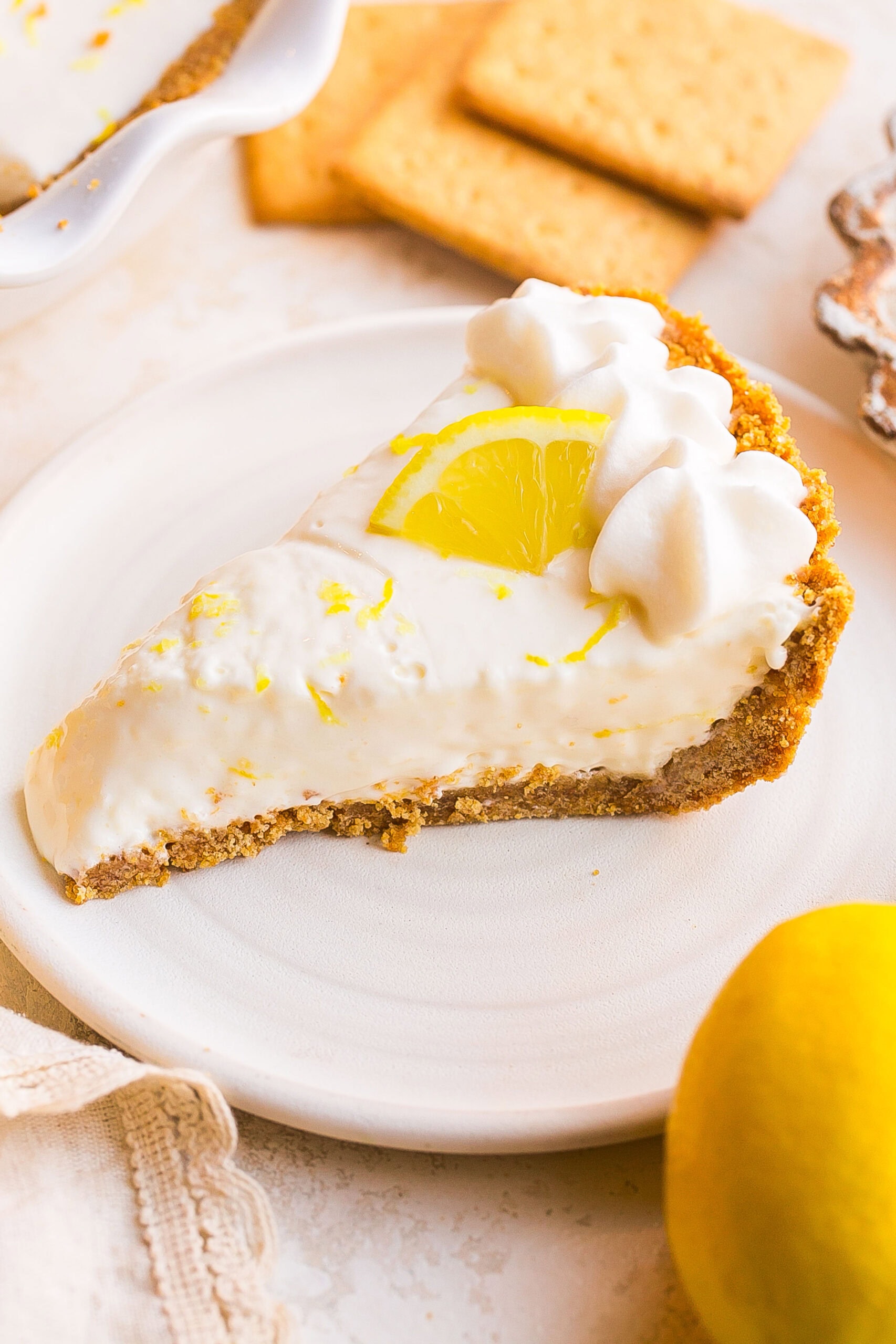 Slice of Lemonade Pie with Cream Cheese topped with whipped cream and lemon zest on a white dessert plate.
