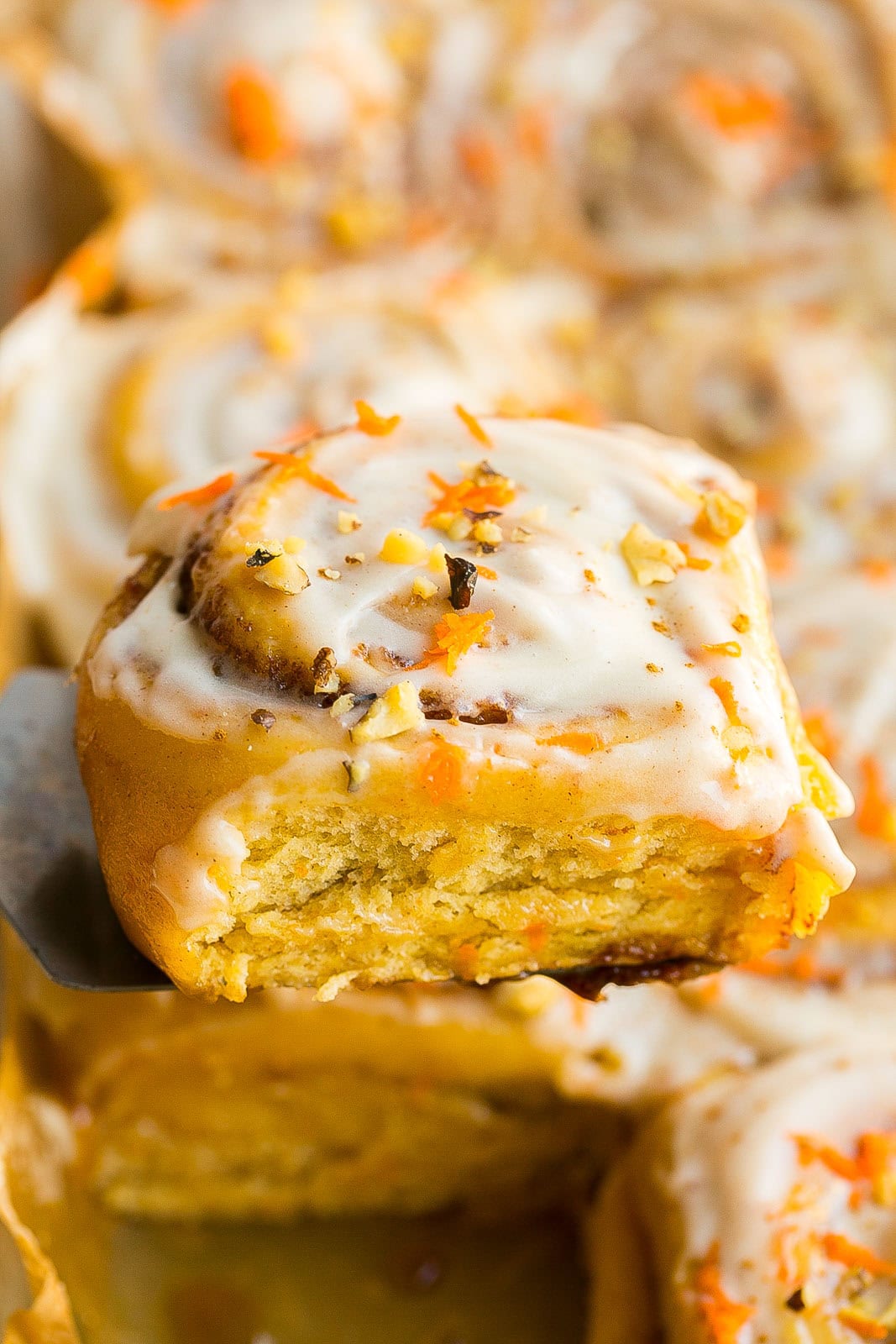 Carrot Cake Cinnamon Roll with on a spatula being pulled from baking dish.