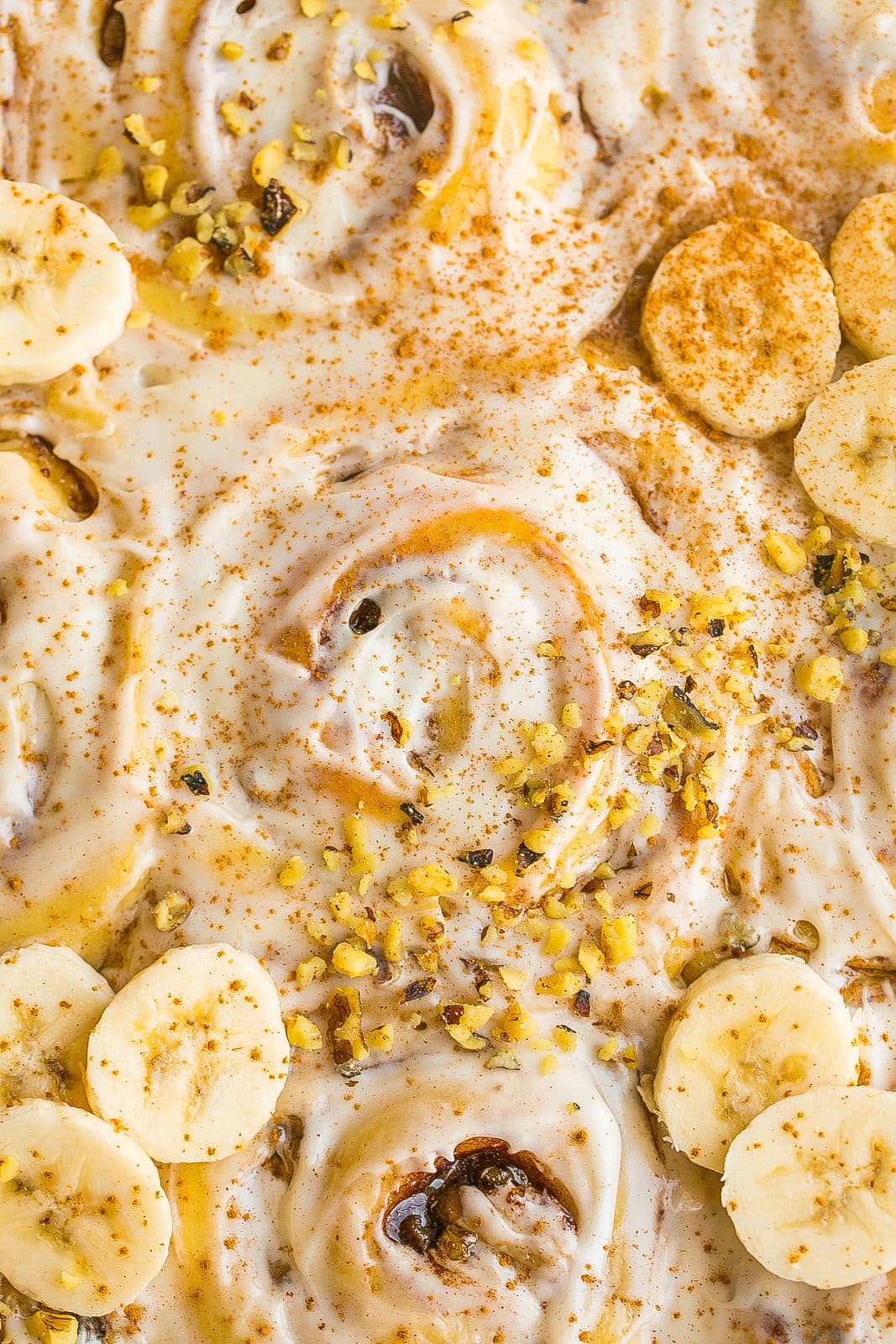 Close up of Banana Bread Cinnamon Rolls topped with cream cheese frosting and sliced bananas and chopped walnuts in a baking dish.