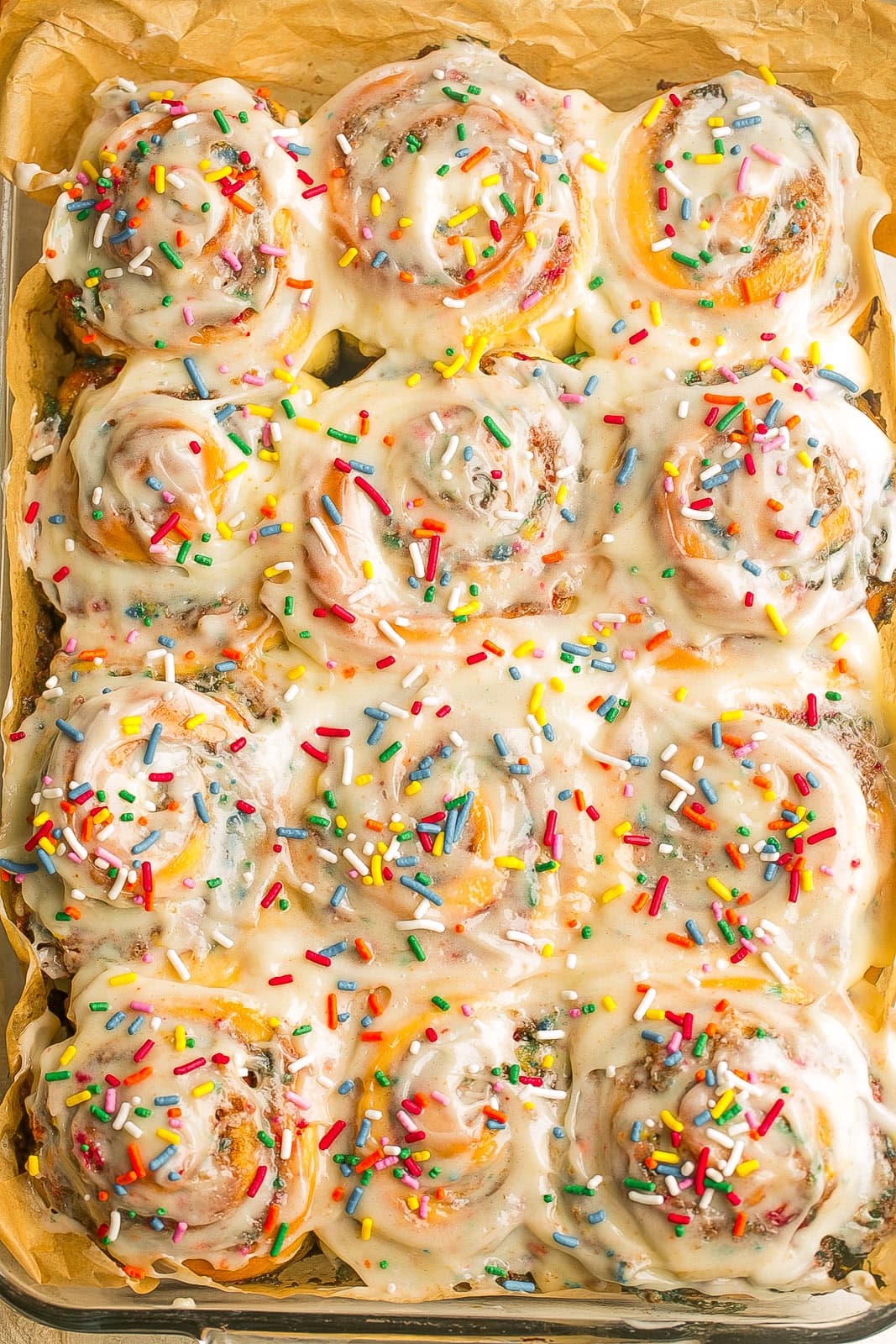 Funfetti cinnamon rolls topped with cream cheese frosting and rainbow sprinkles in a baking dish.
