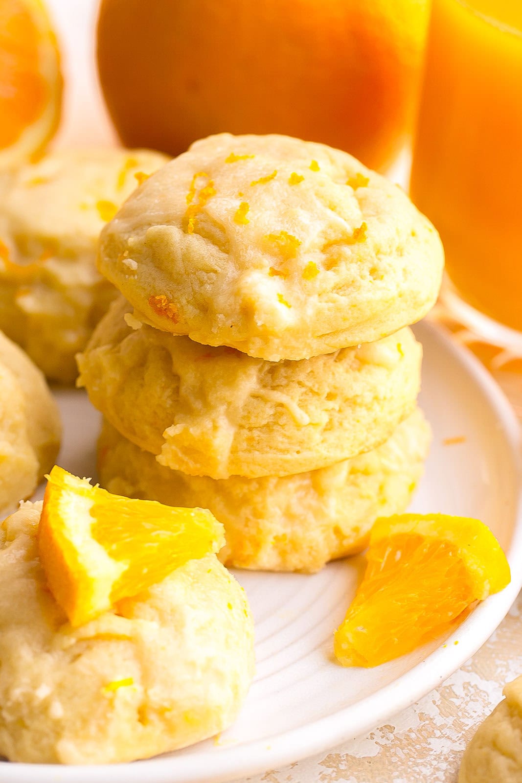Stack of thick orange sugar cookies on a plate with creamy orange icing and zest.