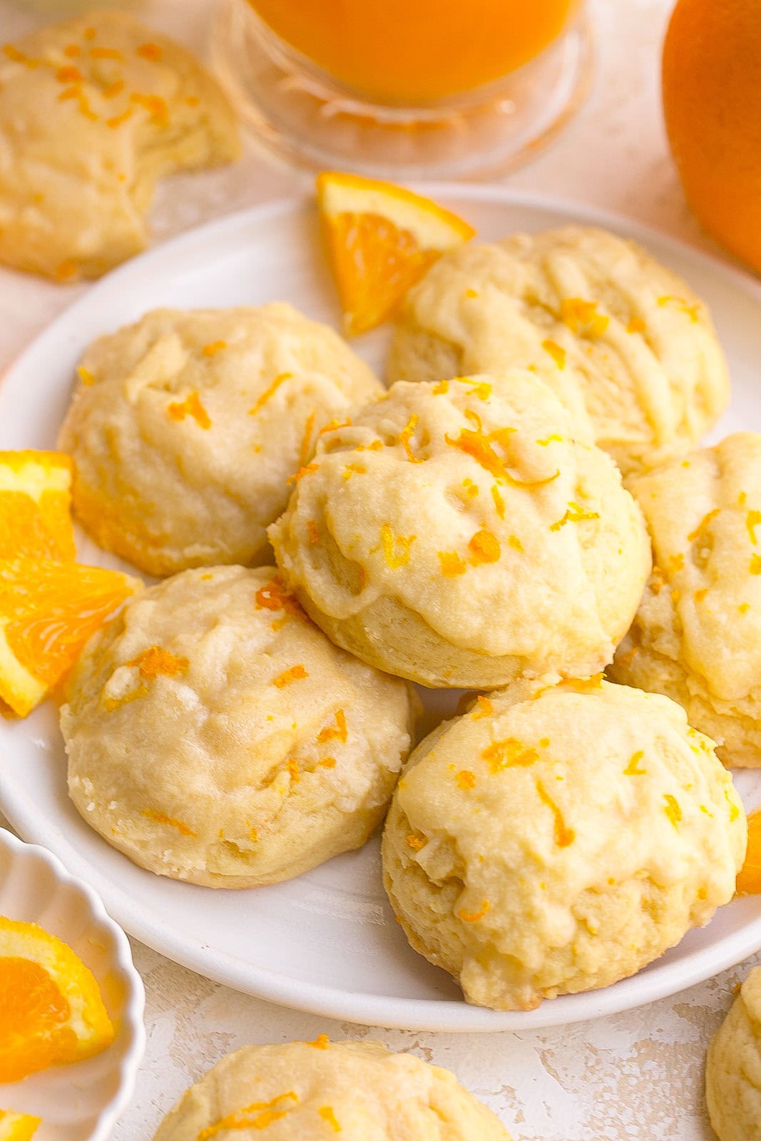 Thick bakery-style orange sugar cookies on a plate with fresh orange zest and glaze.