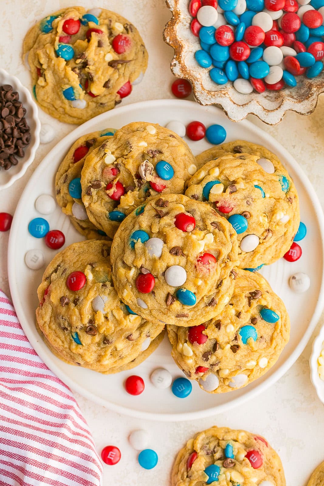 A white plate full of soft bakery-style patriotic chocolate chip cookies with red white and blue candies.