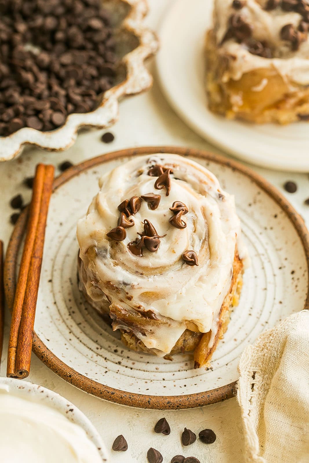 Chocolate Chip Cinnamon Roll on a white plate fresh from the oven with icing and chocolate chips on top.