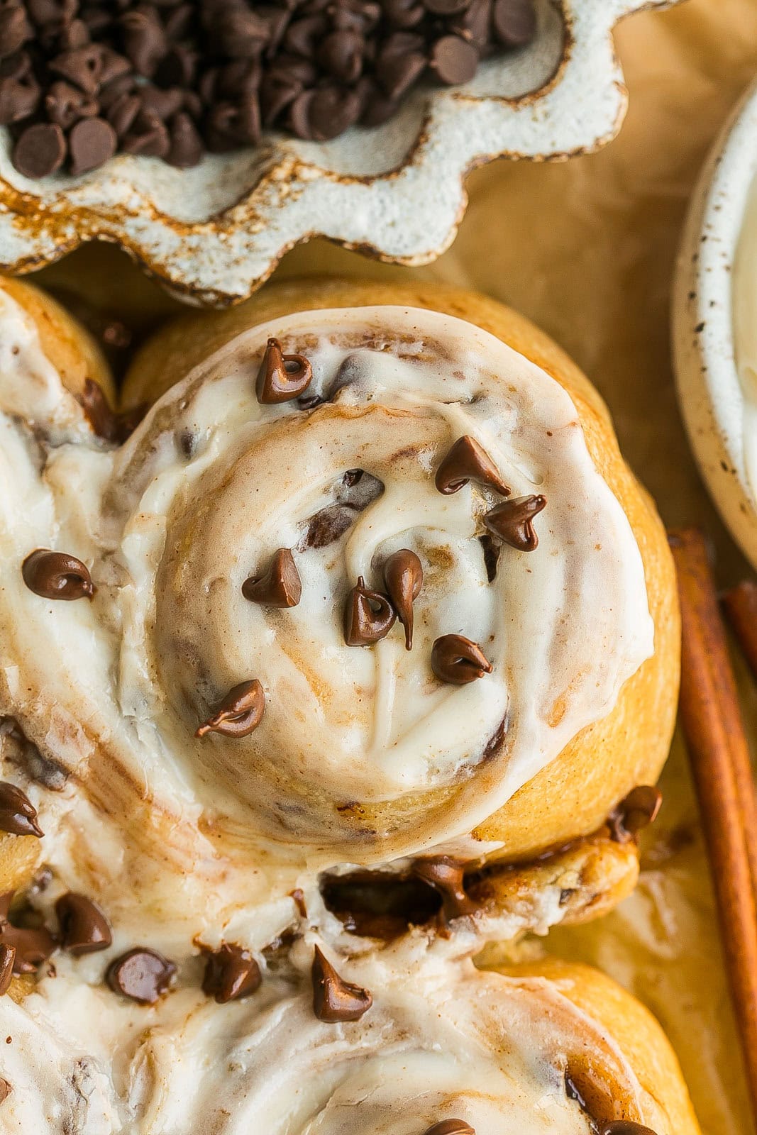 Close up view of a frosted homemade cinnamon roll with mini chocolate chips on top.