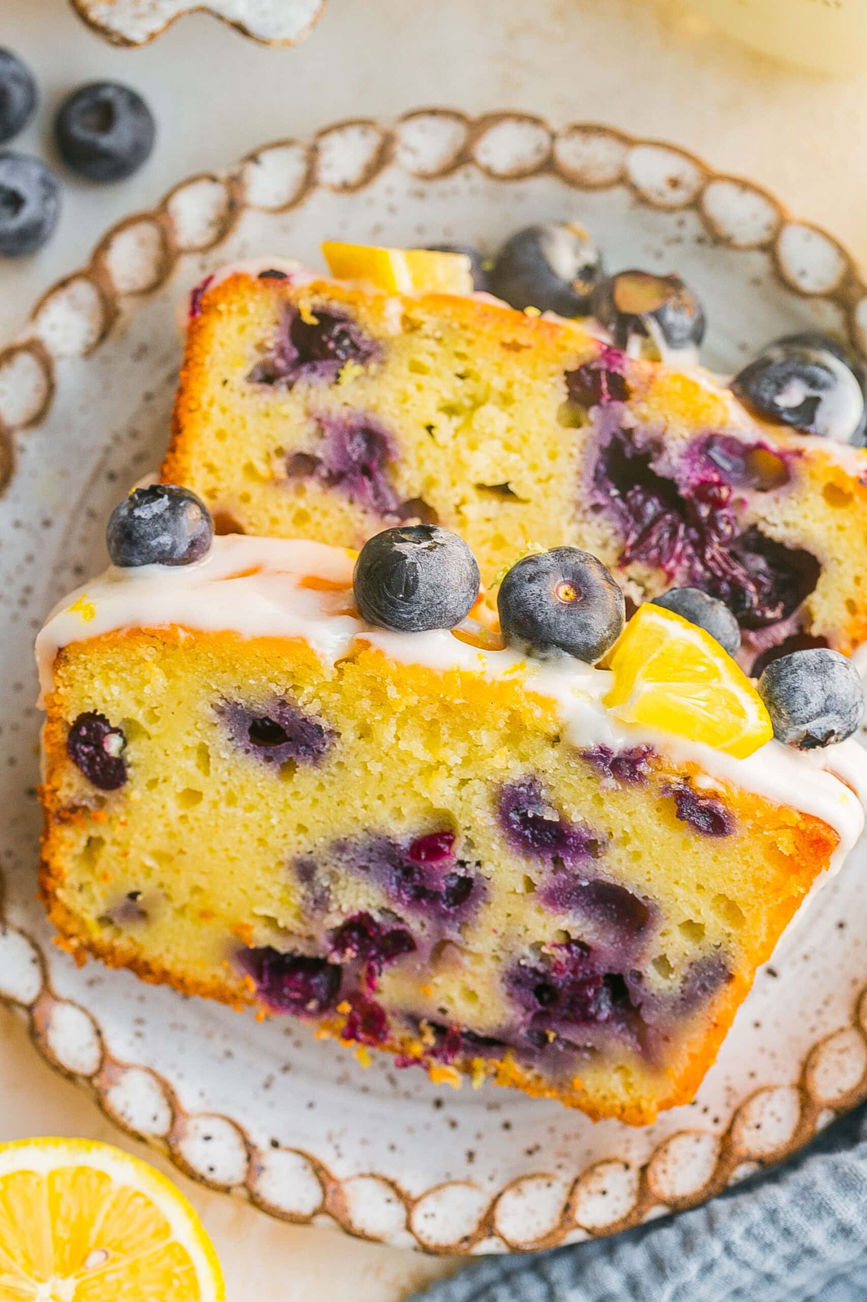 Blueberry Lemon Pound Cake topped with lemon glaze, fresh blueberries, and lemon slices on a plate.