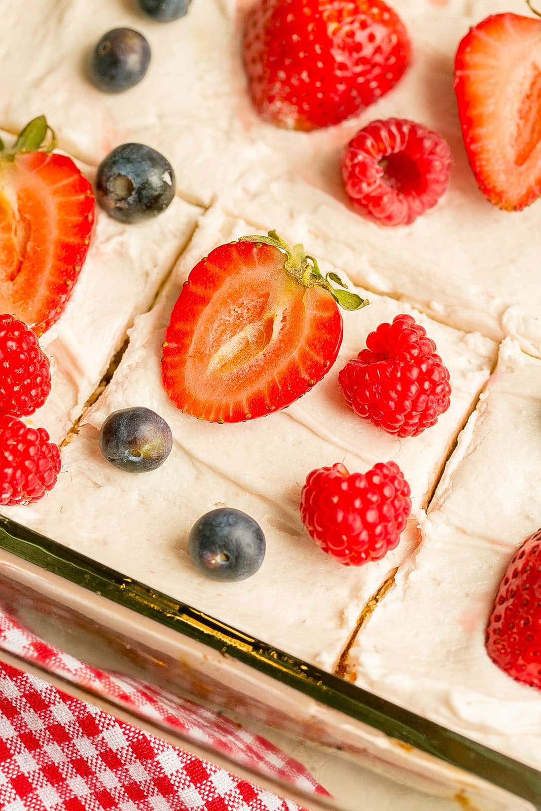 Berry yogurt sheet cake topped with frosting and fresh strawberries, blueberries, and raspberries sliced into squares.